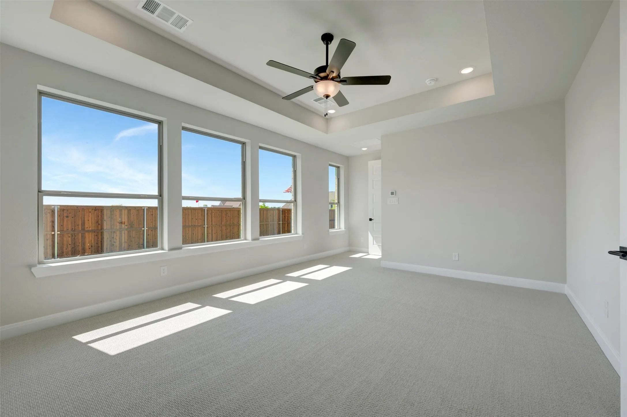 Recessed lighting, ceiling fan, tray ceiling, wall-to-wall carpeting, multiple windows