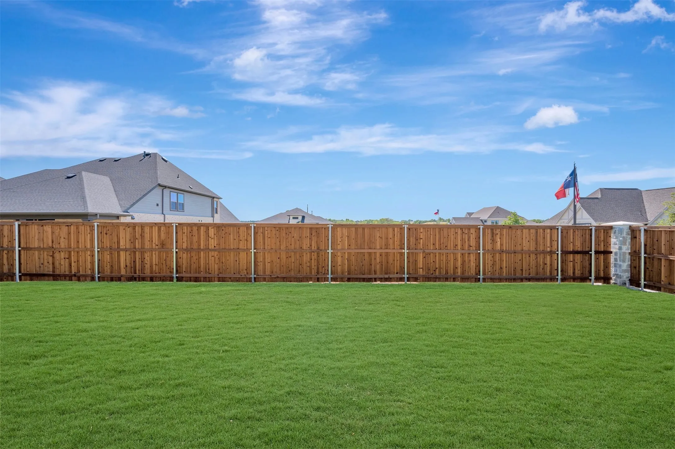 Expansive green lawn with a wood plank privacy fence and stone pillar accent