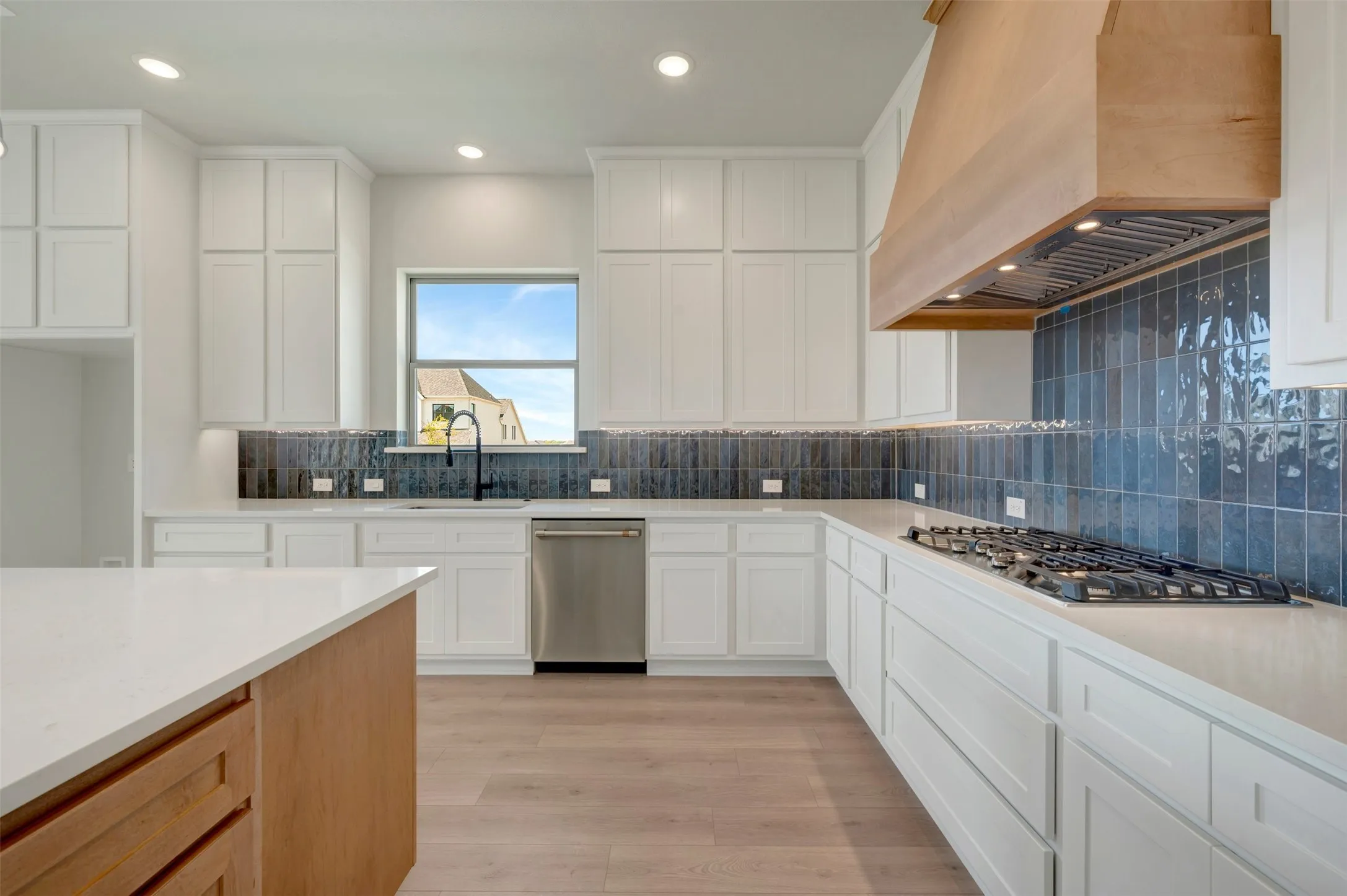 Kitchen featuring abundant white cabinetry, light wood-finish flooring, an island with a light-toned countertop, a blue tile backsplash, and a wood-finish range hood