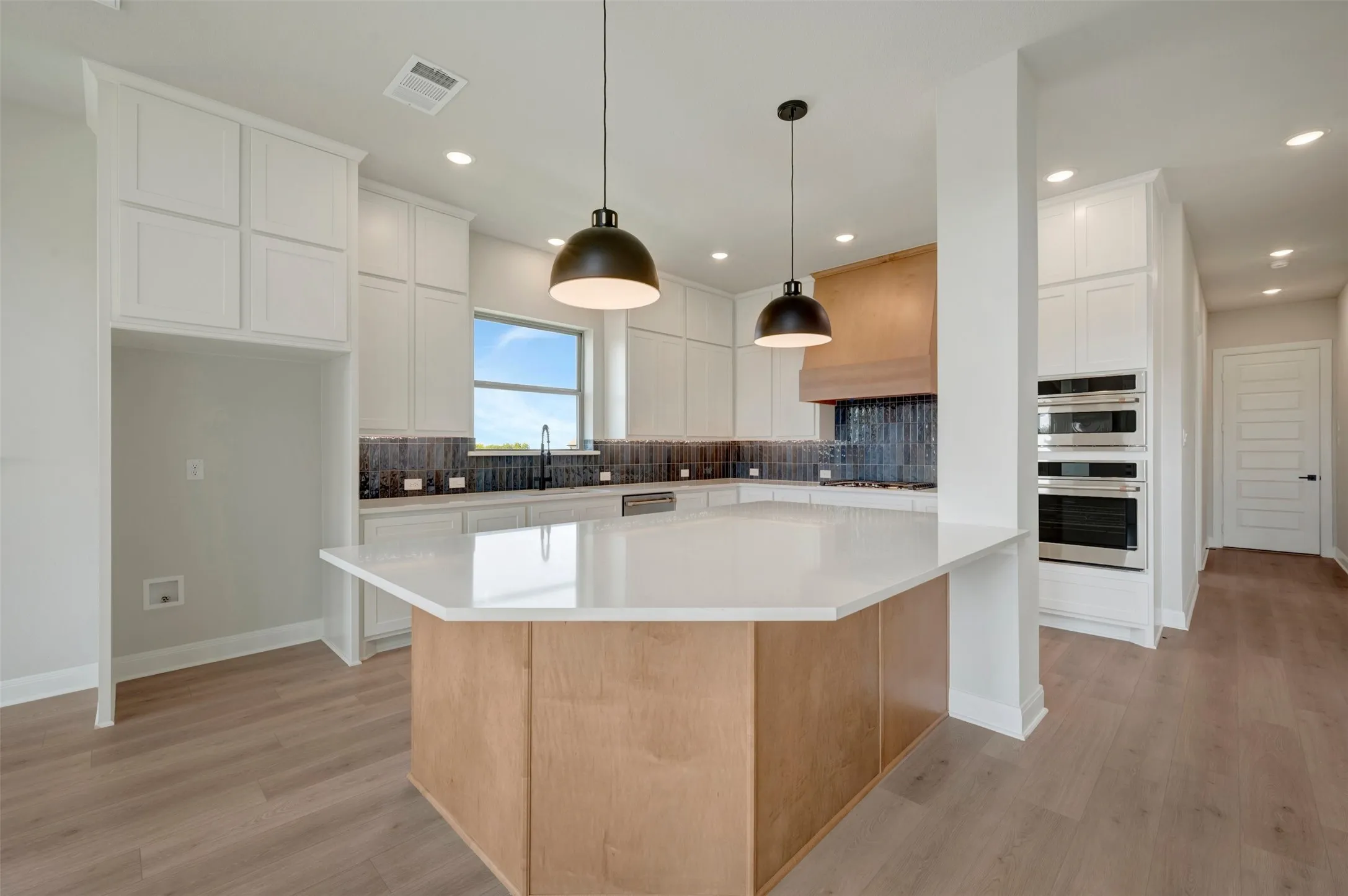 Kitchen featuring light wood-finish flooring, white cabinetry, a wood-paneled range hood, and a central island with a light-toned countertop