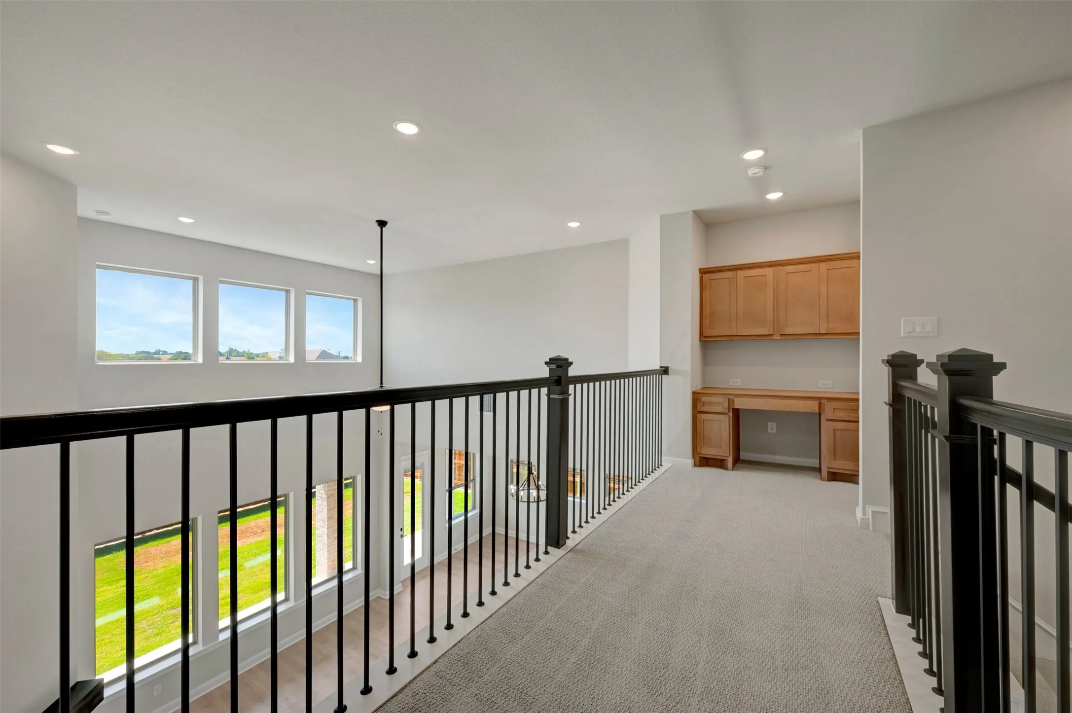 Upper level loft with built-in desk, wood-finish cabinetry, recessed lighting, and multiple windows