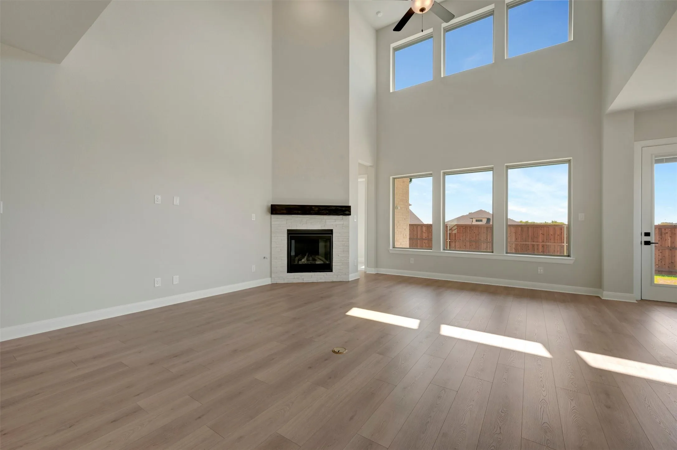 Two-story living area featuring wood-finish flooring, a corner fireplace with a dark wood mantel, high ceilings, large windows, and a ceiling fan