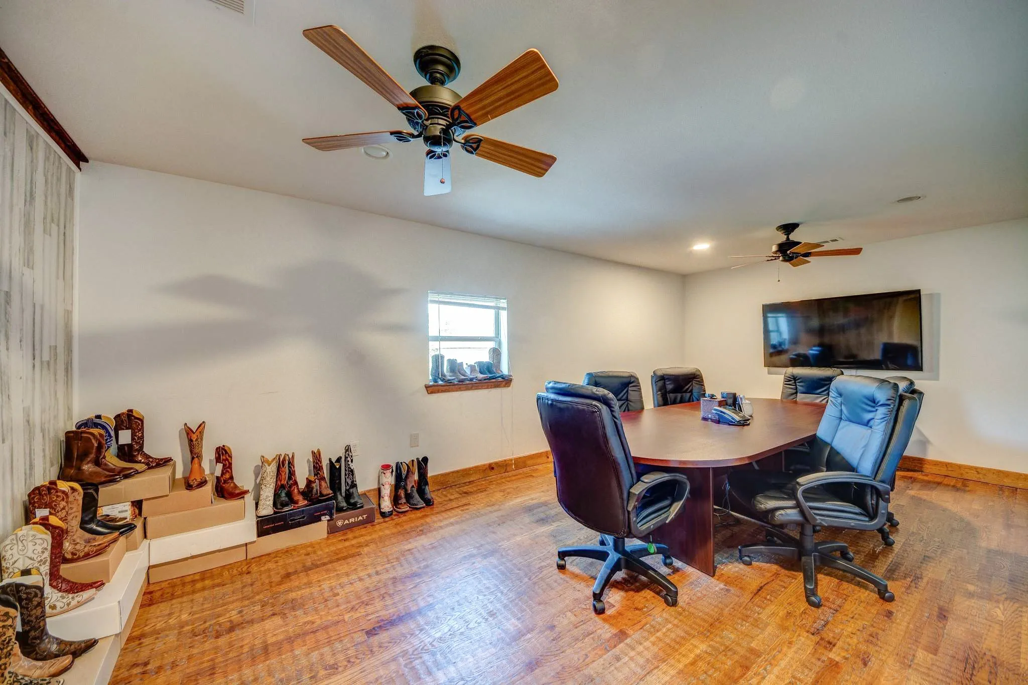 Spacious room featuring wood-finish flooring, white walls, and two ceiling fans with integrated lighting
