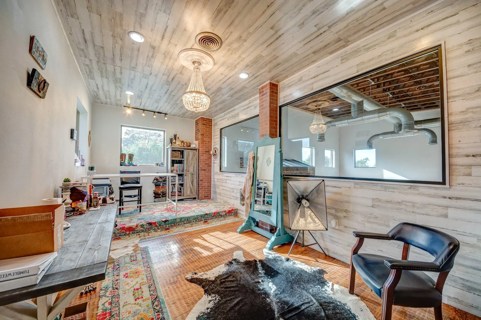 Room featuring wood-finish flooring, white shiplap walls and ceiling, a large interior window, and exposed brick accents