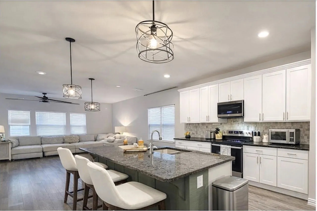 Open-concept kitchen and living area featuring a large center island with seating, white shaker cabinetry, stainless steel appliances, and wood-finish flooring