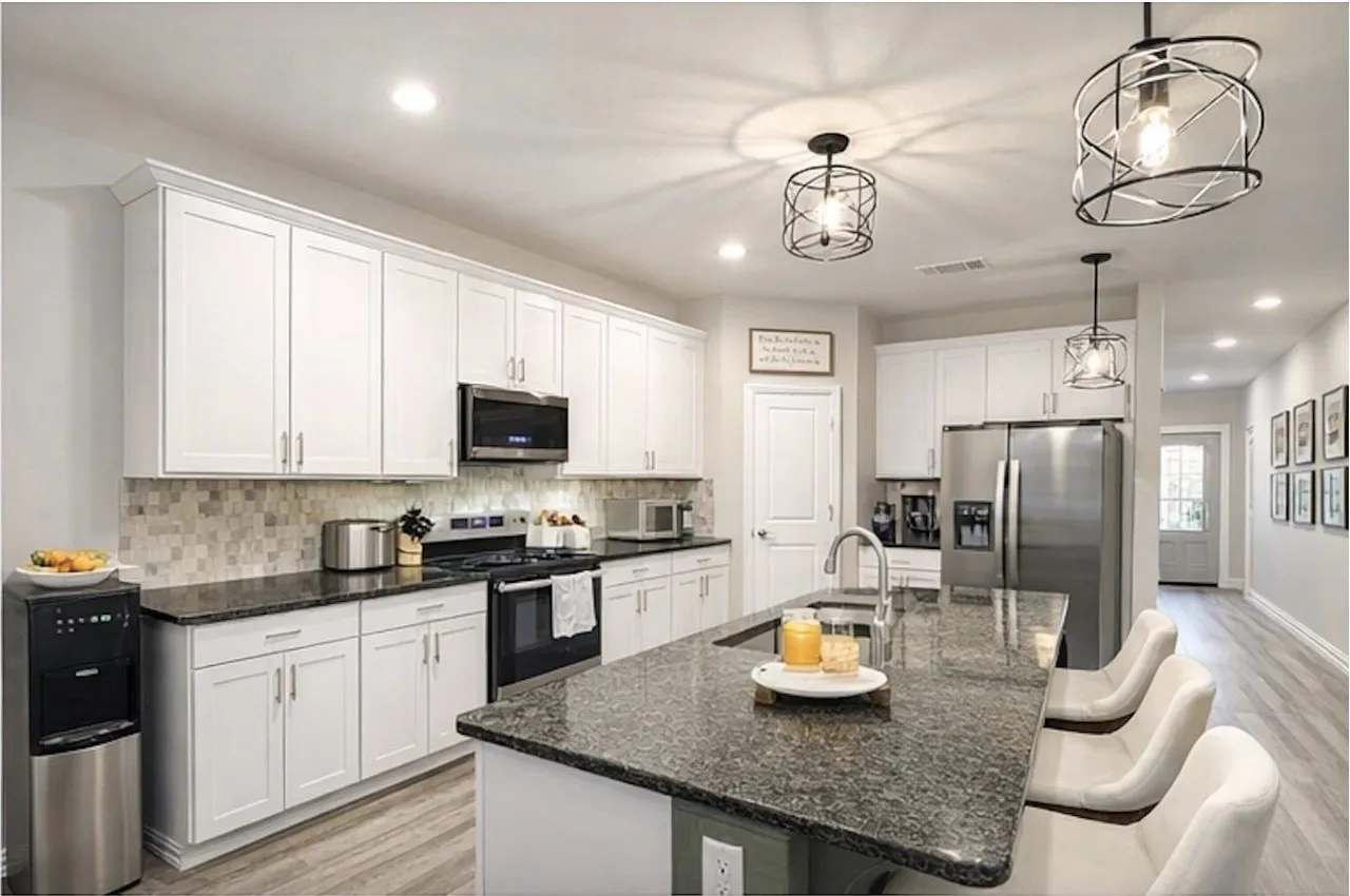 Modern kitchen featuring white cabinetry, dark stone countertops, stainless steel appliances, and a mosaic tile backsplash