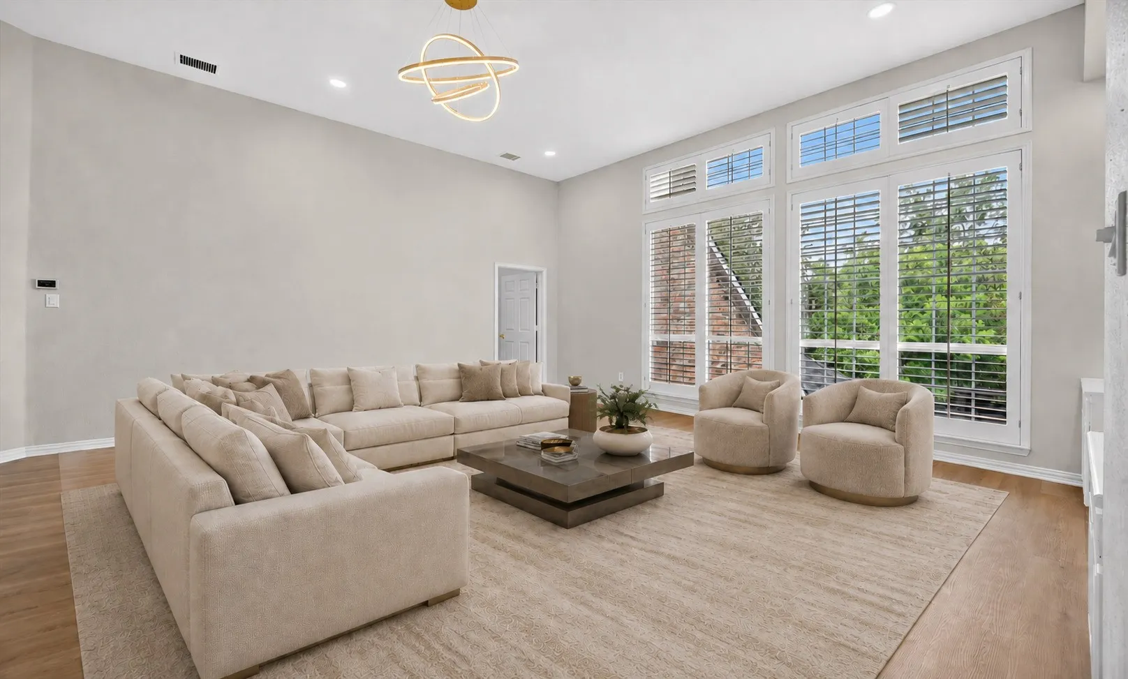 Spacious living area featuring expansive windows with plantation shutters, vaulted ceilings, recessed lighting, and wood-finish flooring