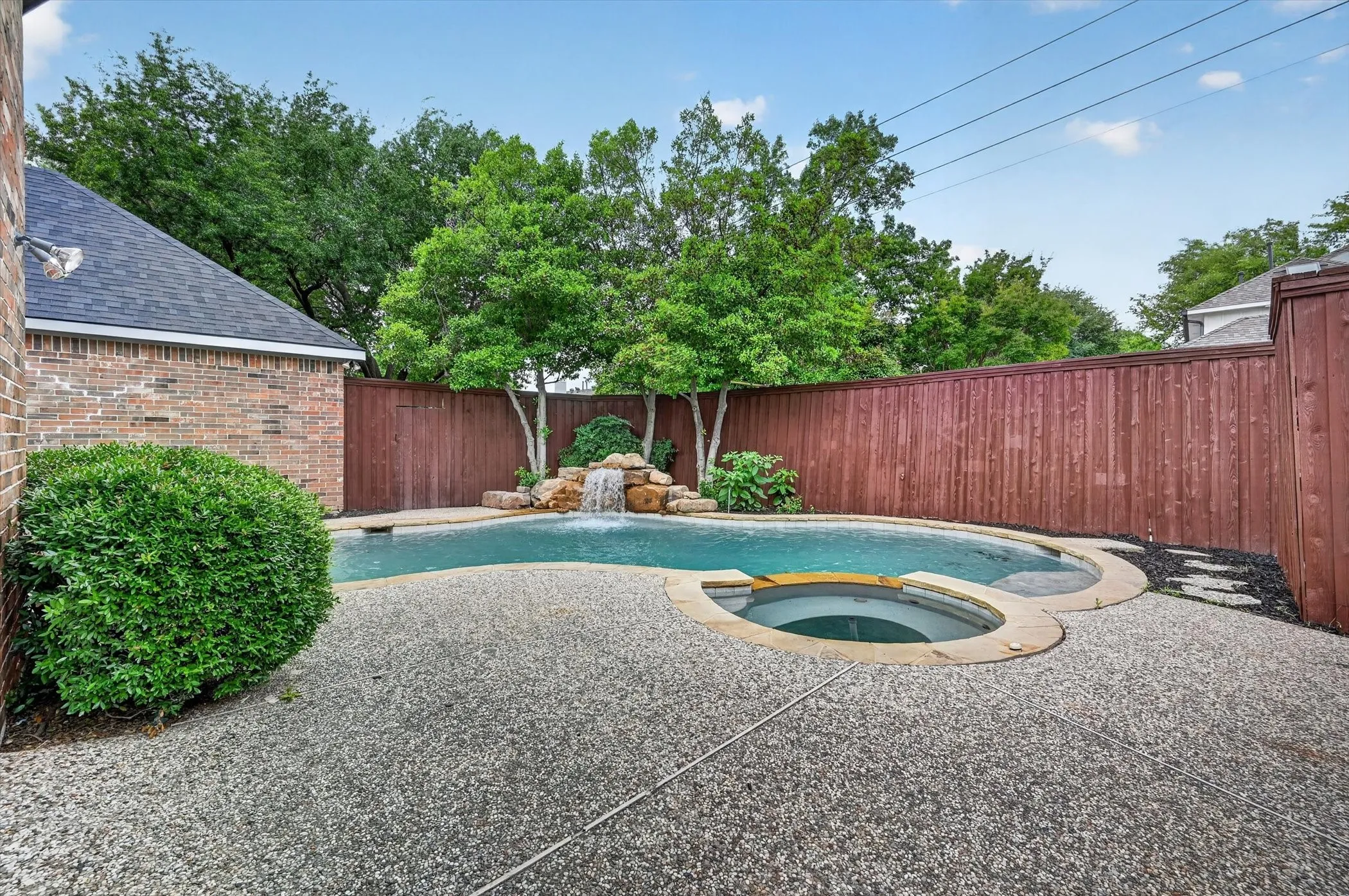 Rear yard featuring a freeform swimming pool with rock waterfall, integrated spa, and exposed aggregate concrete decking