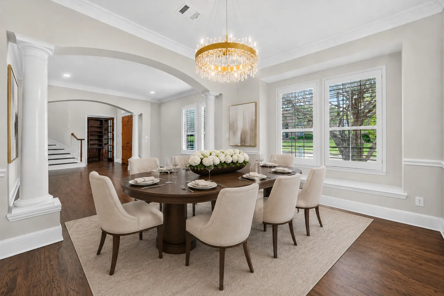 Formal dining area featuring rich wood-finish flooring, a tiered crystal chandelier, and white plantation shutters