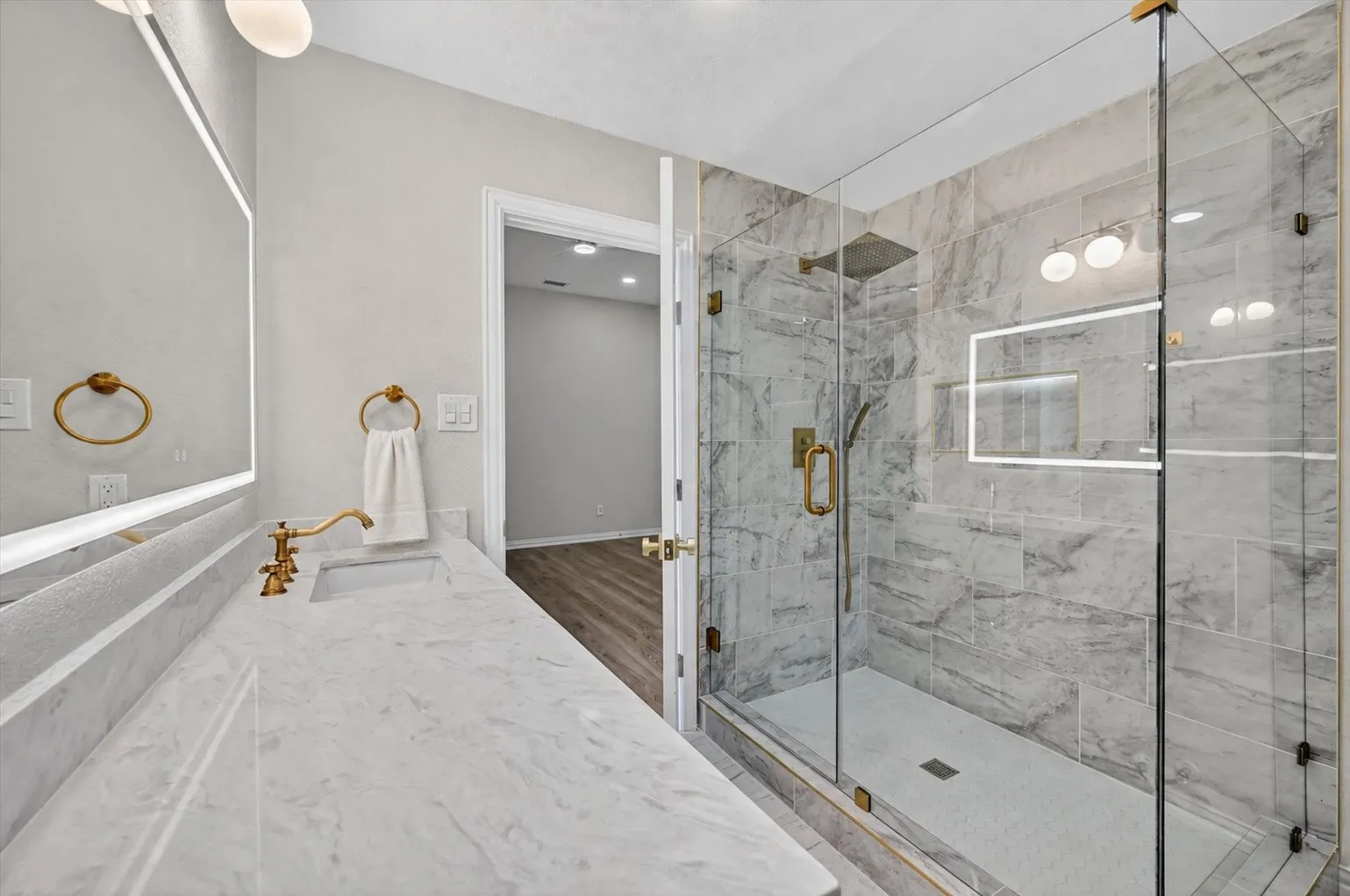 Contemporary bathroom featuring a spacious glass-enclosed shower with gold-tone fixtures, a built-in shower niche, and large format wall tiling