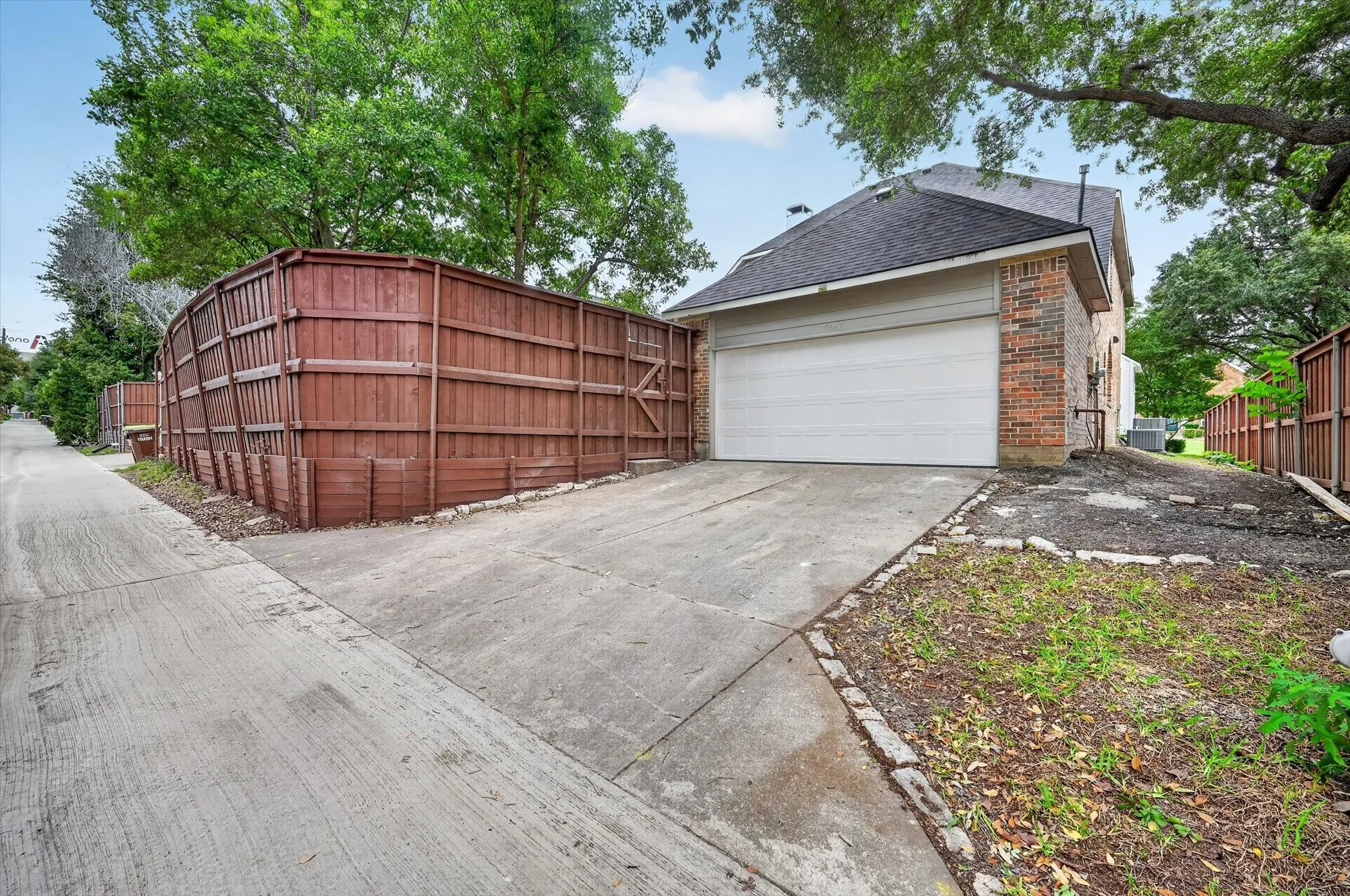 Side-entry garage with an attached concrete driveway, brick exterior, and a dark shingle roof