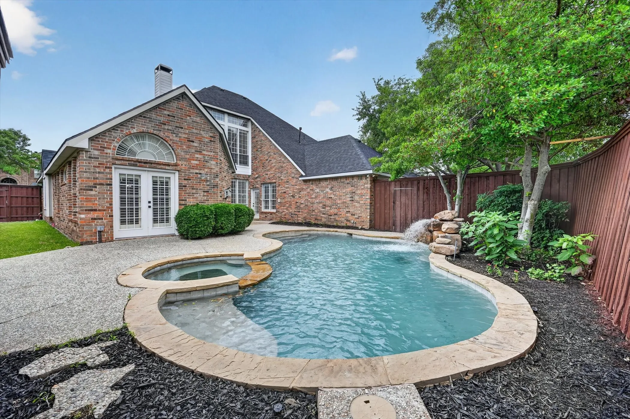 Backyard oasis featuring a curvilinear pool with an integrated spa and rock waterfall