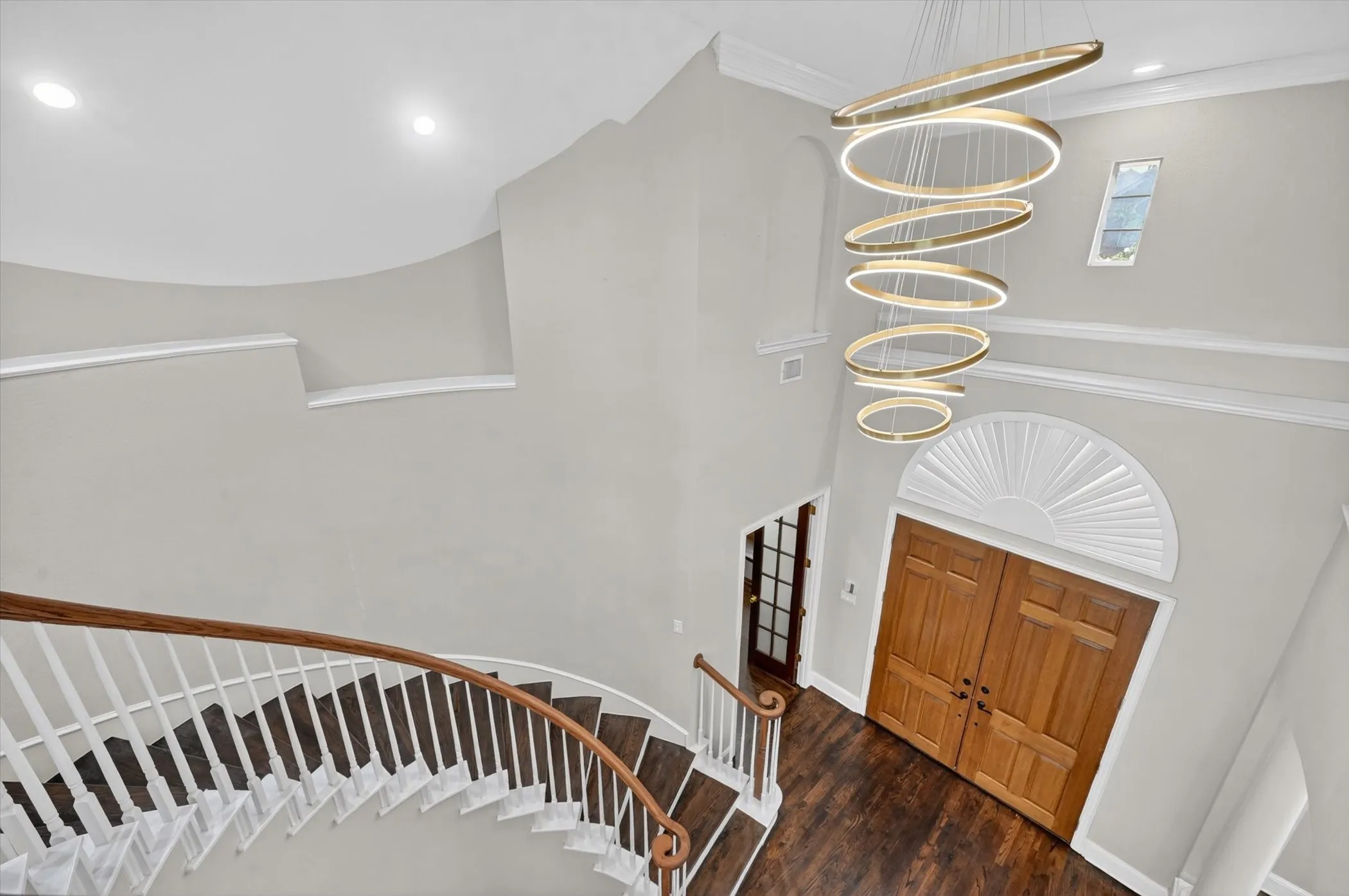 Grand entryway featuring a curved staircase with wood-finish treads and white risers, a multi-tiered circular chandelier, double wood-paneled entry doors, and an arched fanlight window