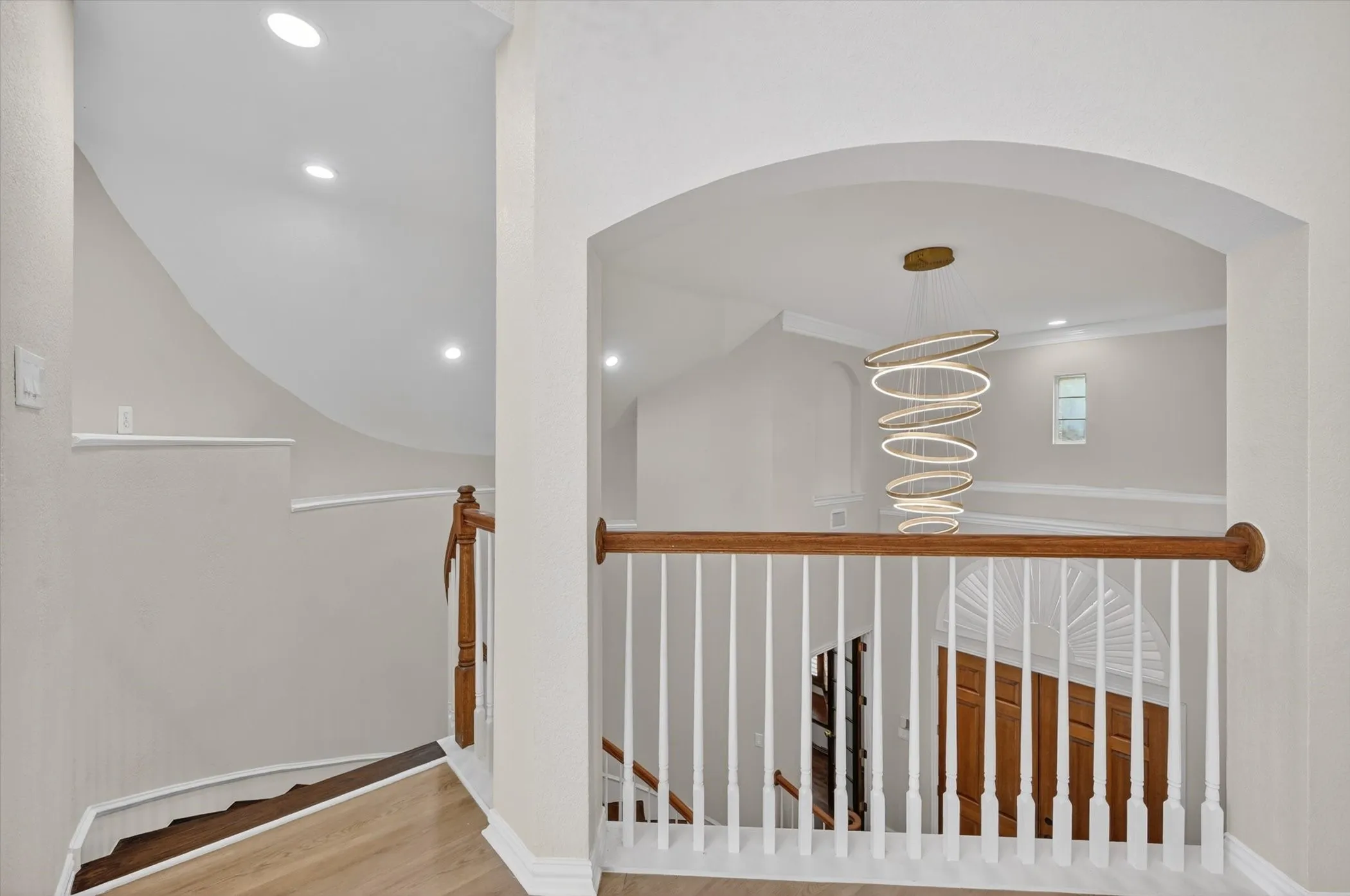 Upper landing featuring light wood-finish flooring and an arched entryway