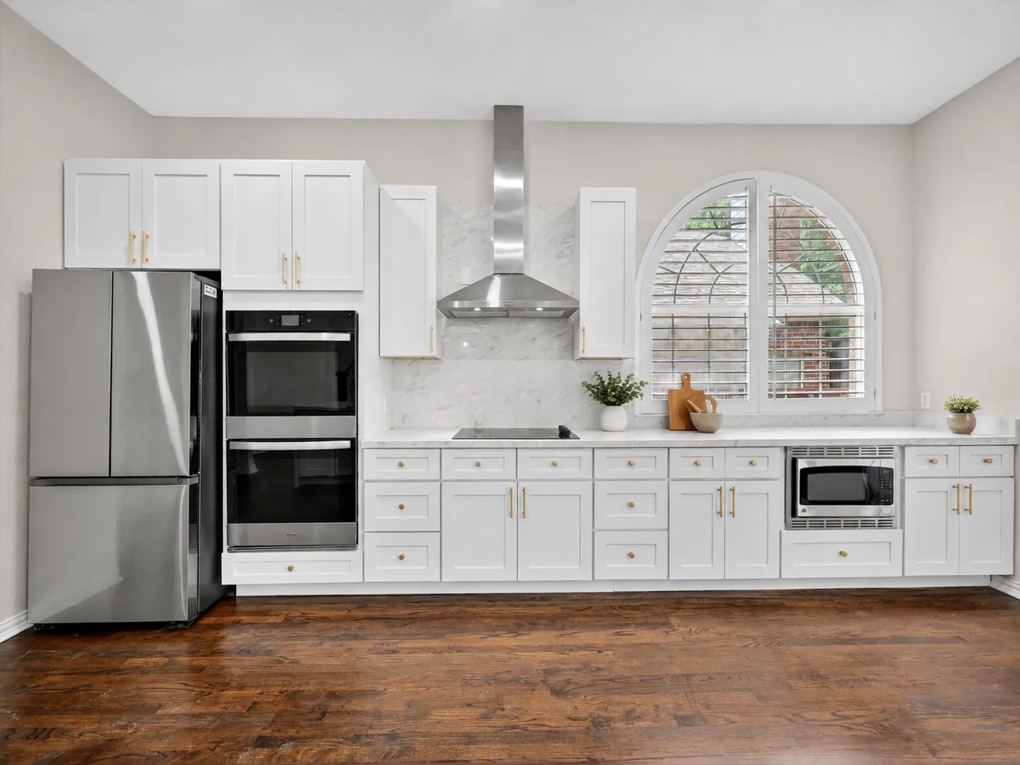 Modern kitchen featuring white cabinetry, stainless steel appliances, marble-look backsplash, and wood-finish flooring
