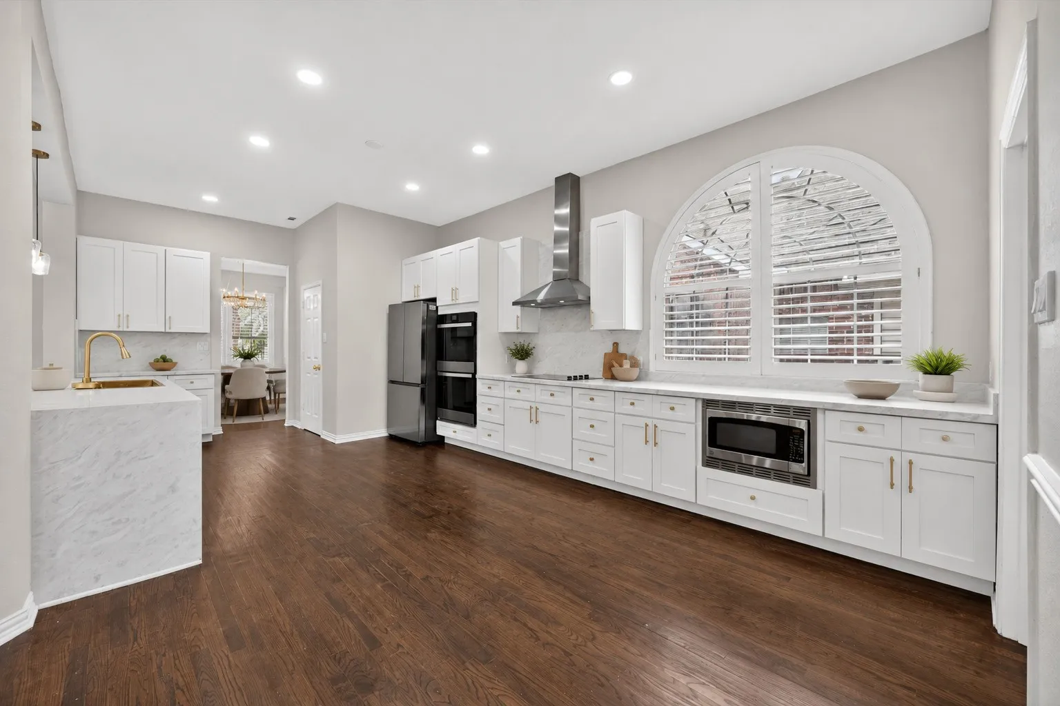 Spacious kitchen featuring rich wood-finish flooring and an expansive arched window with plantation shutters