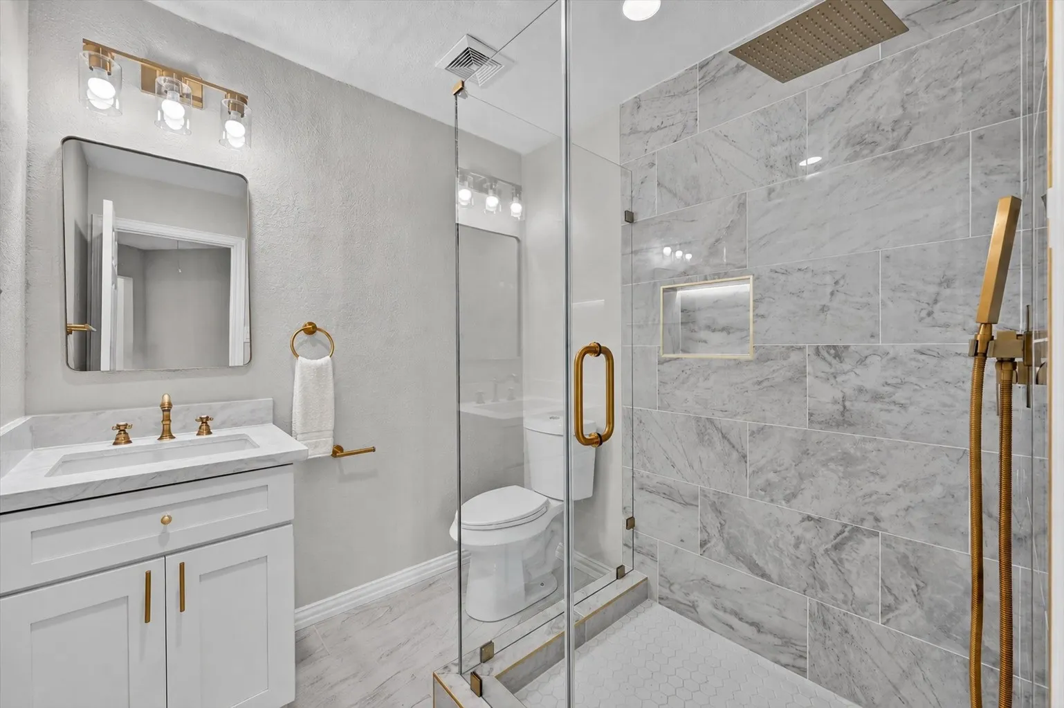 Bathroom featuring a glass-enclosed shower with large-format stone-look tile, a built-in shower niche, and a gold-finish rainfall showerhead