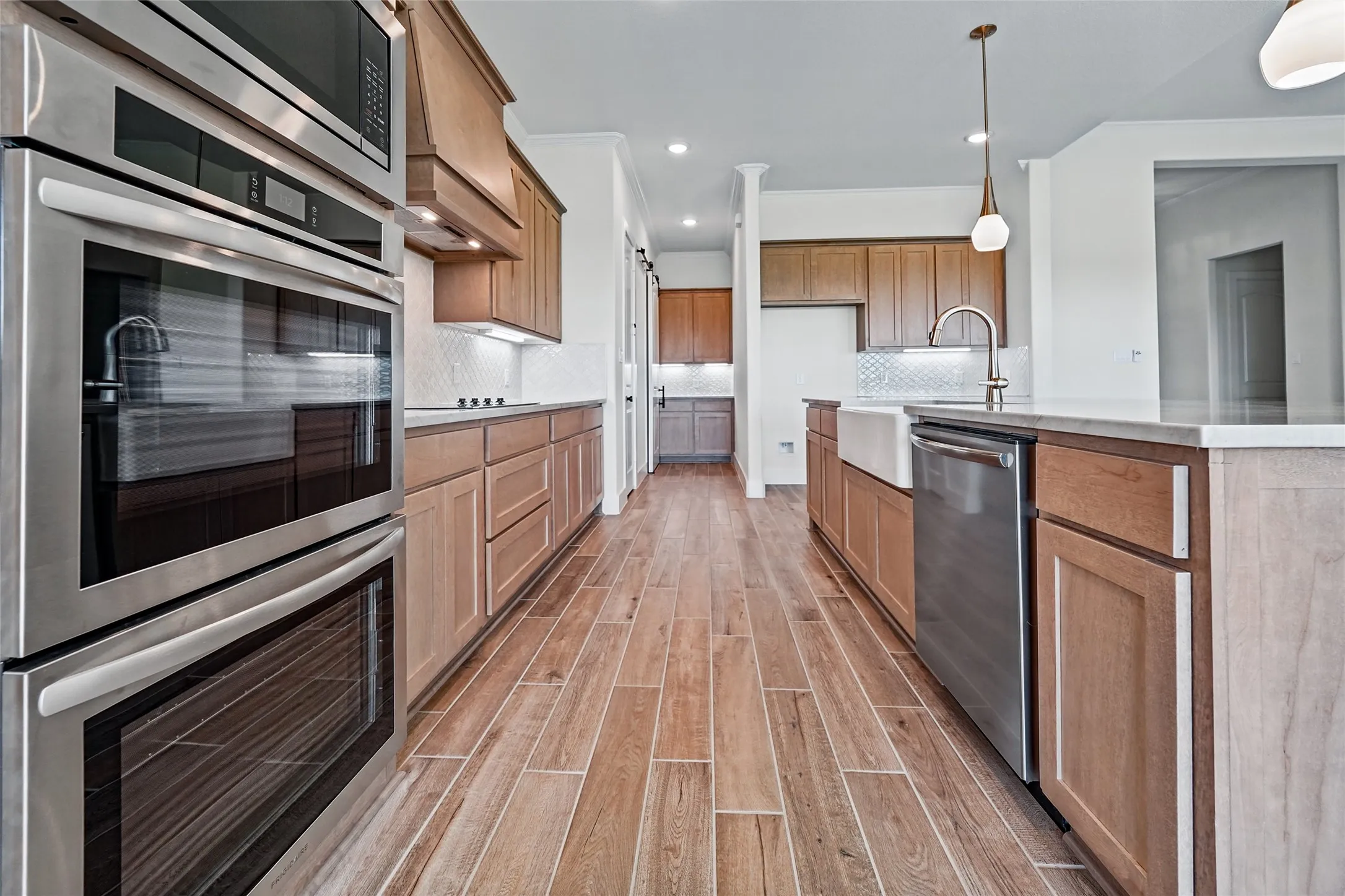 Stainless steel double ovens, wood-finish flooring, white subway tile backsplash, stainless steel microwave, and built-in shaker-style cabinetry