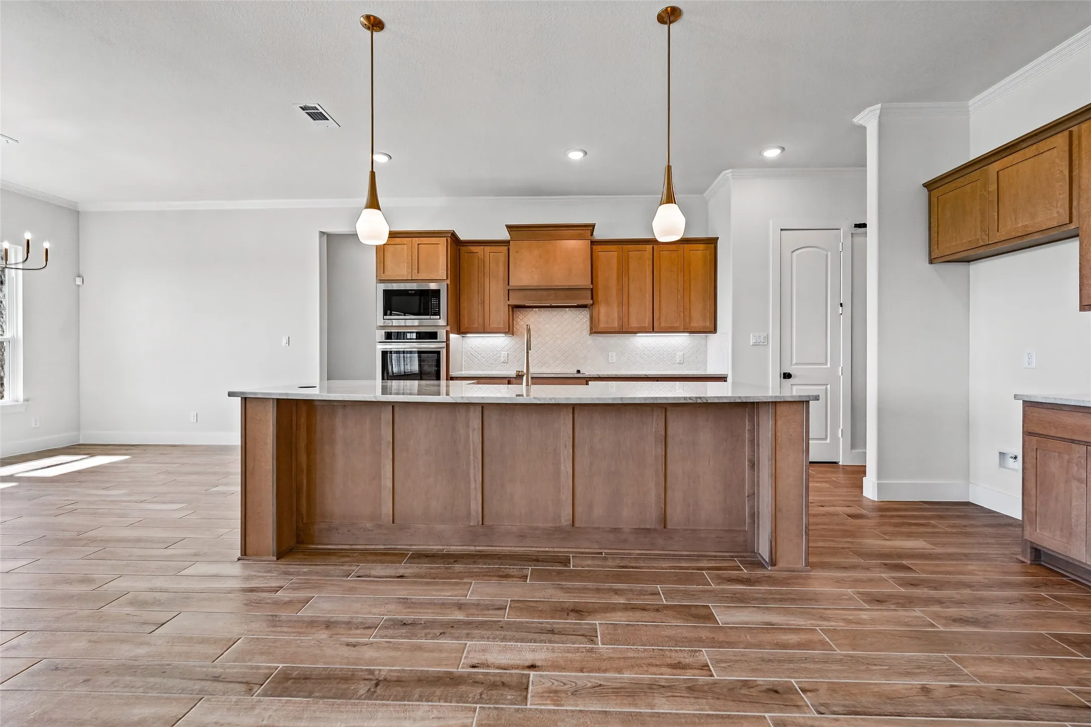 Kitchen featuring wood-finish flooring, a large island with a light-toned countertop, built-in stainless steel appliances, wood cabinetry, and pendant lighting