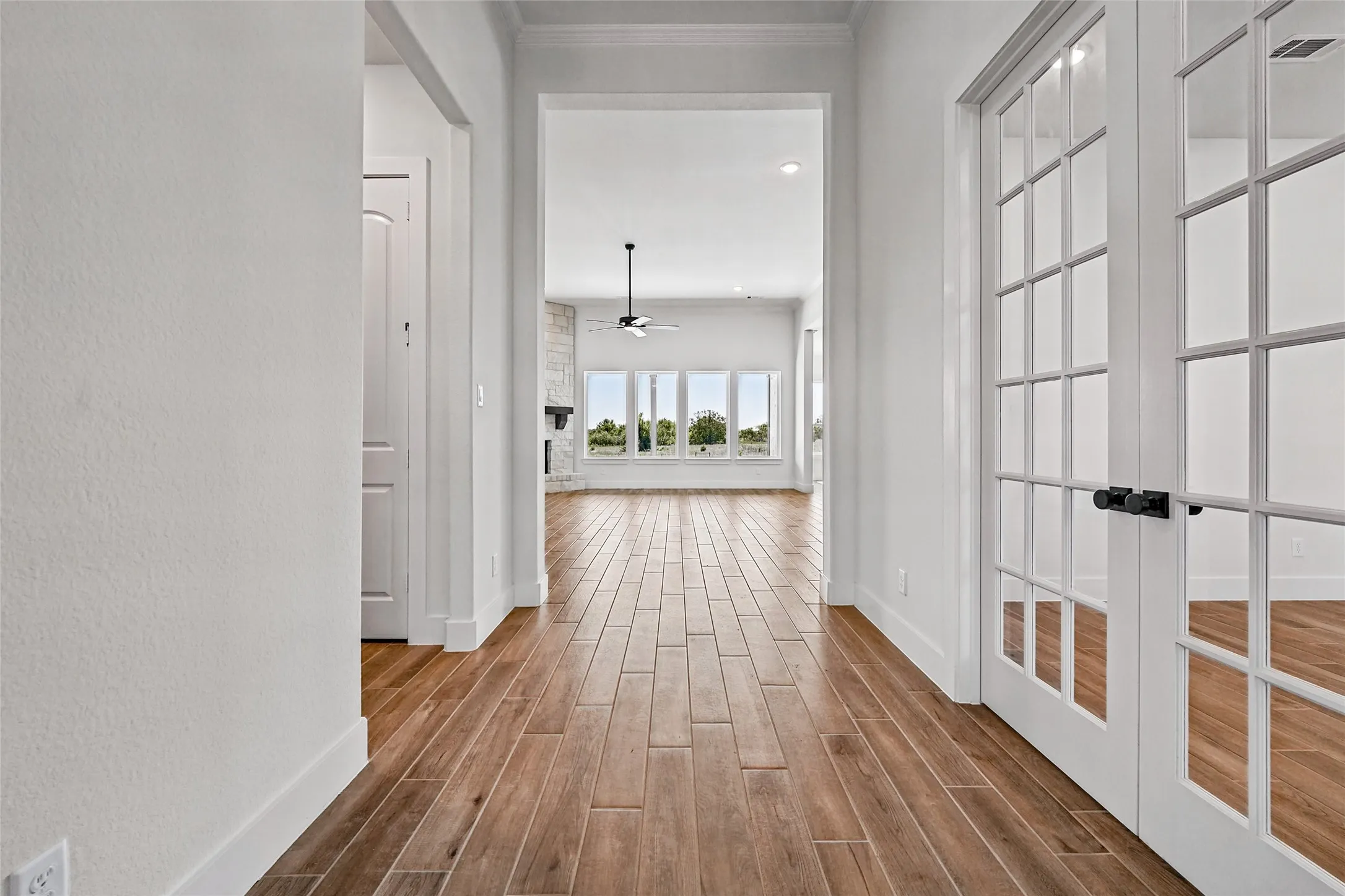 Wood-finish flooring, white walls, and French doors with black hardware