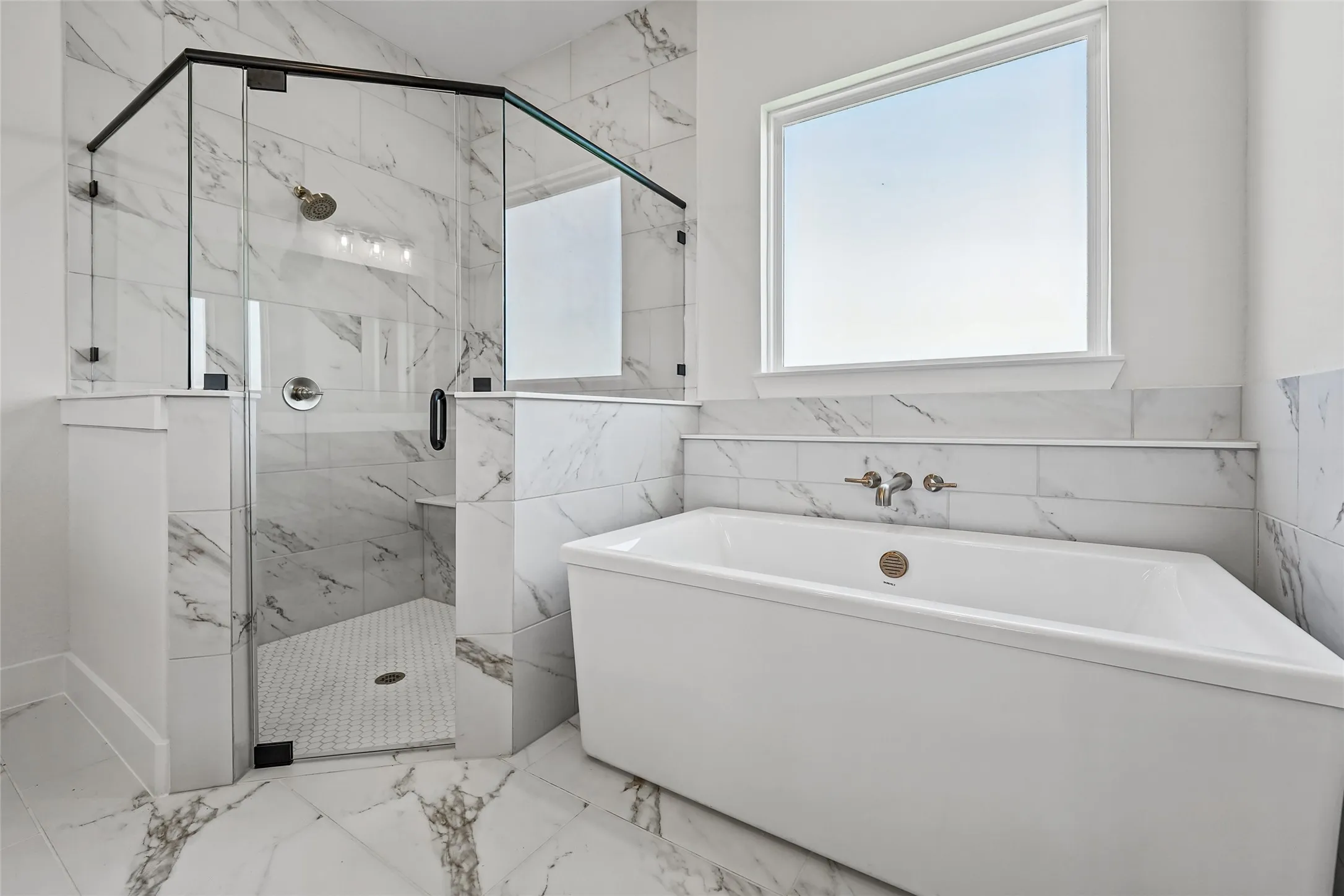 Spacious bathroom featuring a freestanding soaking tub, large window, and a glass-enclosed shower with marble-look tile surround and hex-tile flooring