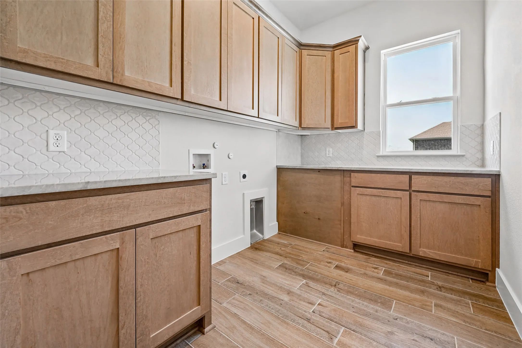 Wood-finish tile flooring, extensive wood cabinetry, light countertops, patterned tile backsplash, and a large window