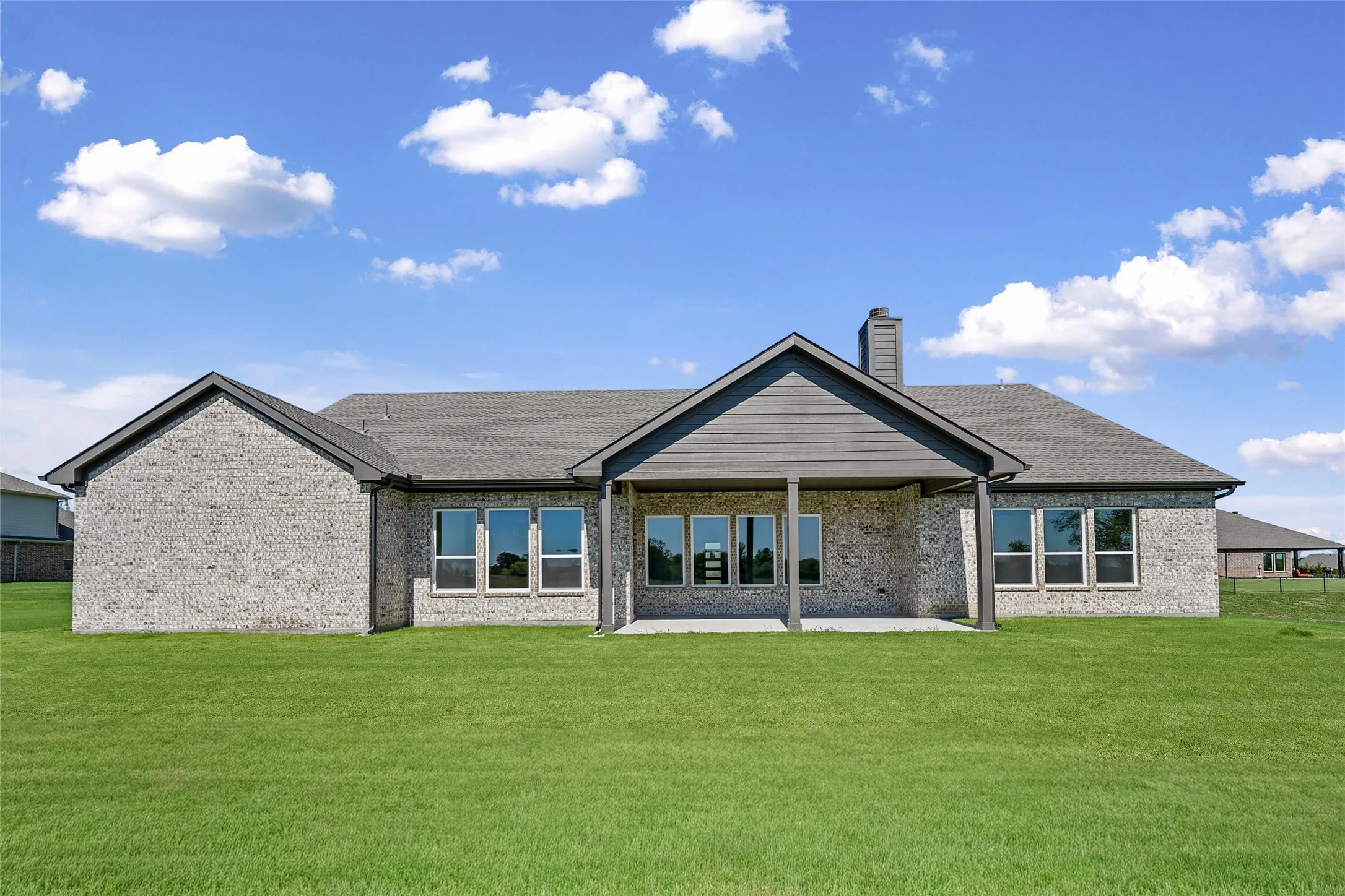 Expansive green lawn, brick exterior, covered patio, multiple windows, and a shingled roof