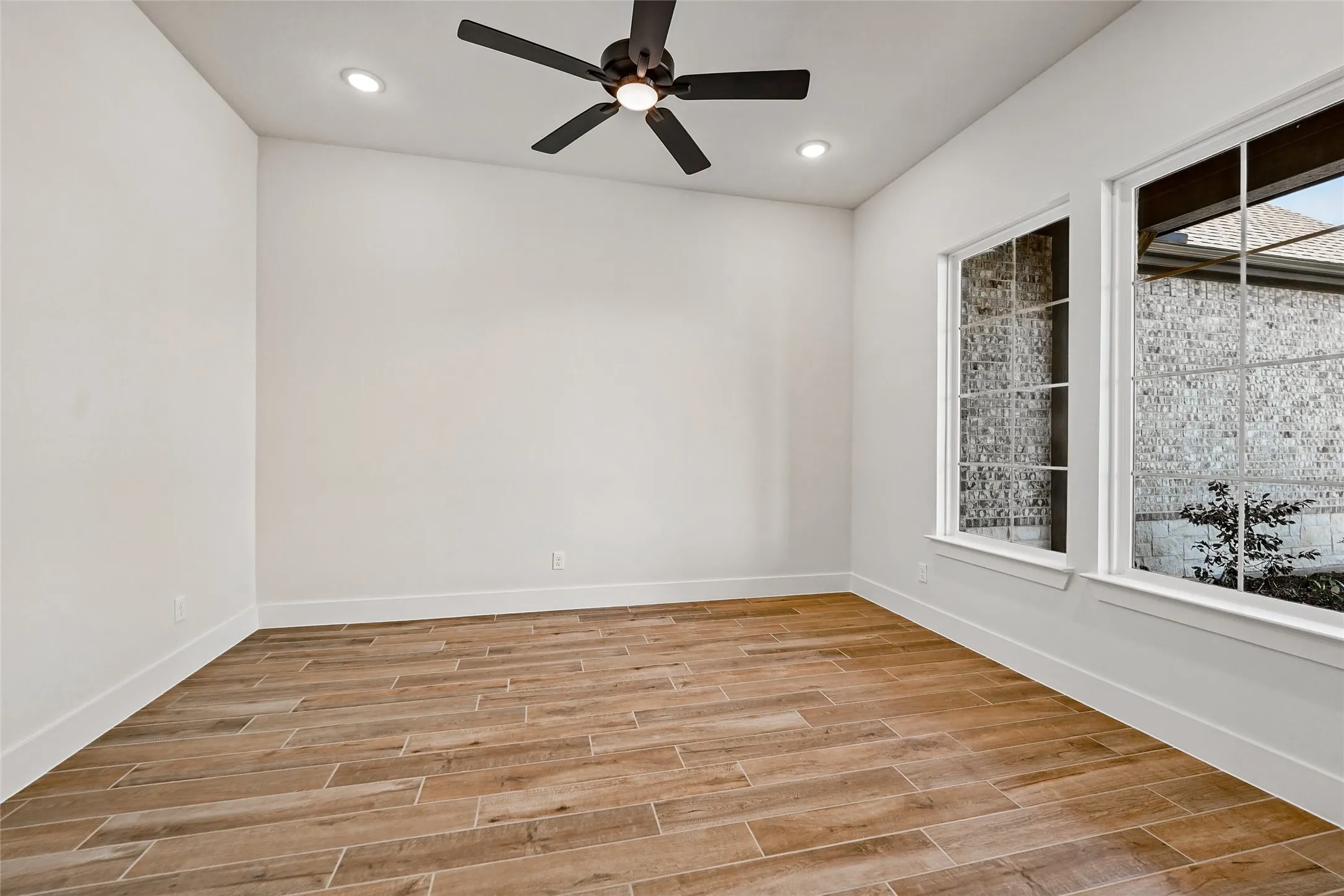 Wood-finish flooring, white walls, two large windows, recessed lighting, and a ceiling fan with integrated lighting