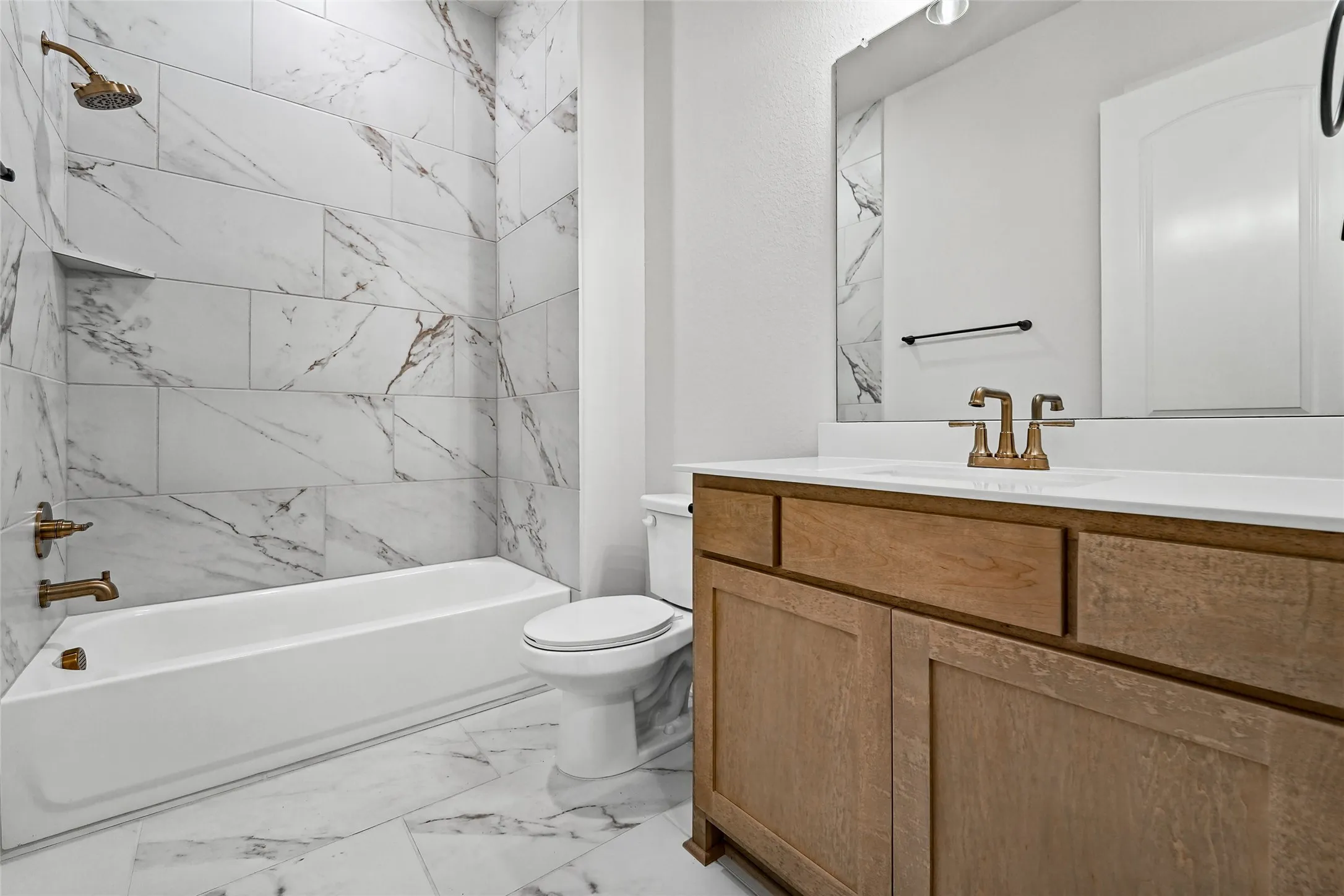 White subway tile shower surround with integrated niche, white bathtub, wood-finish vanity with countertop, and bronze-finish fixtures