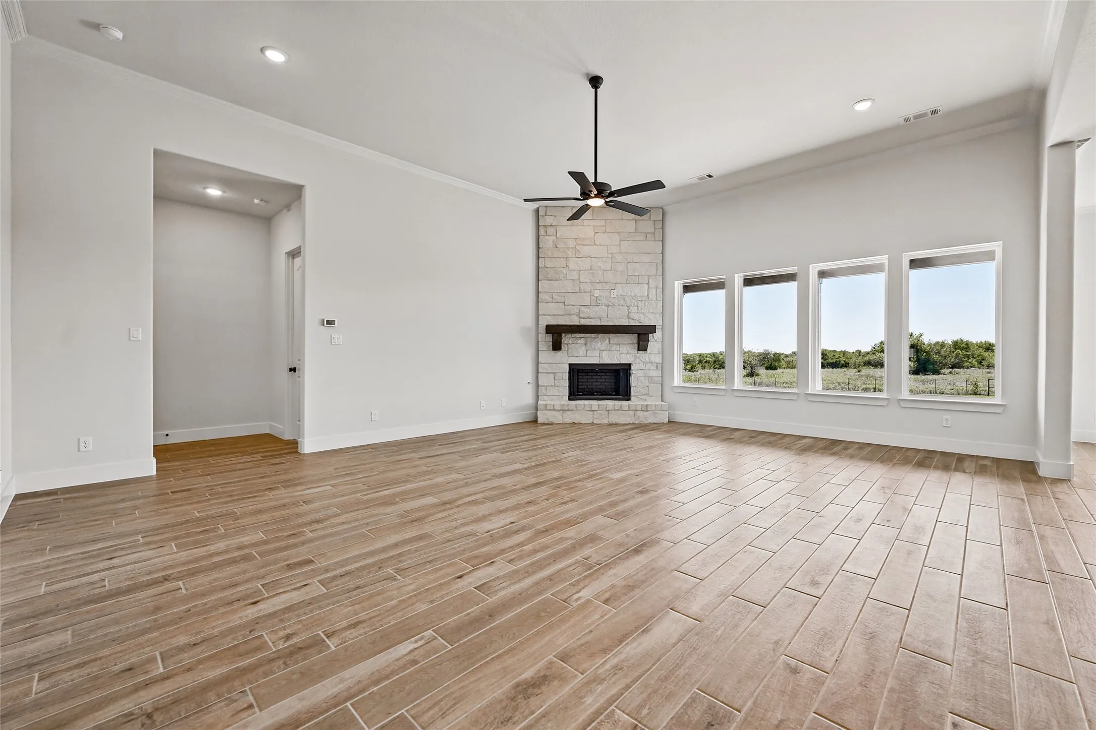 Spacious living area featuring wood-finish tile flooring, a stone-surround fireplace with a wood mantle, and a ceiling fan