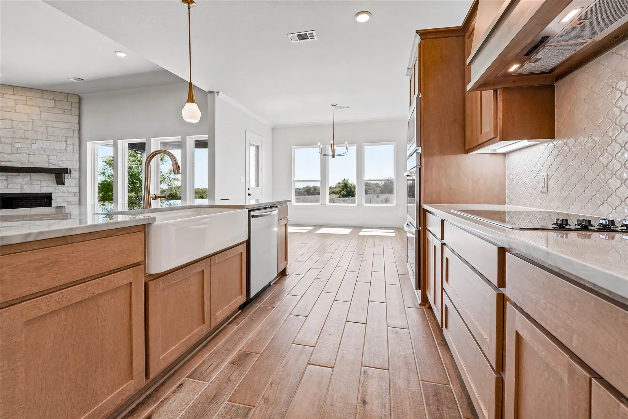 Kitchen featuring wood-finish flooring, light-toned cabinetry, a large farmhouse sink, integrated cooktop, and a patterned tile backsplash