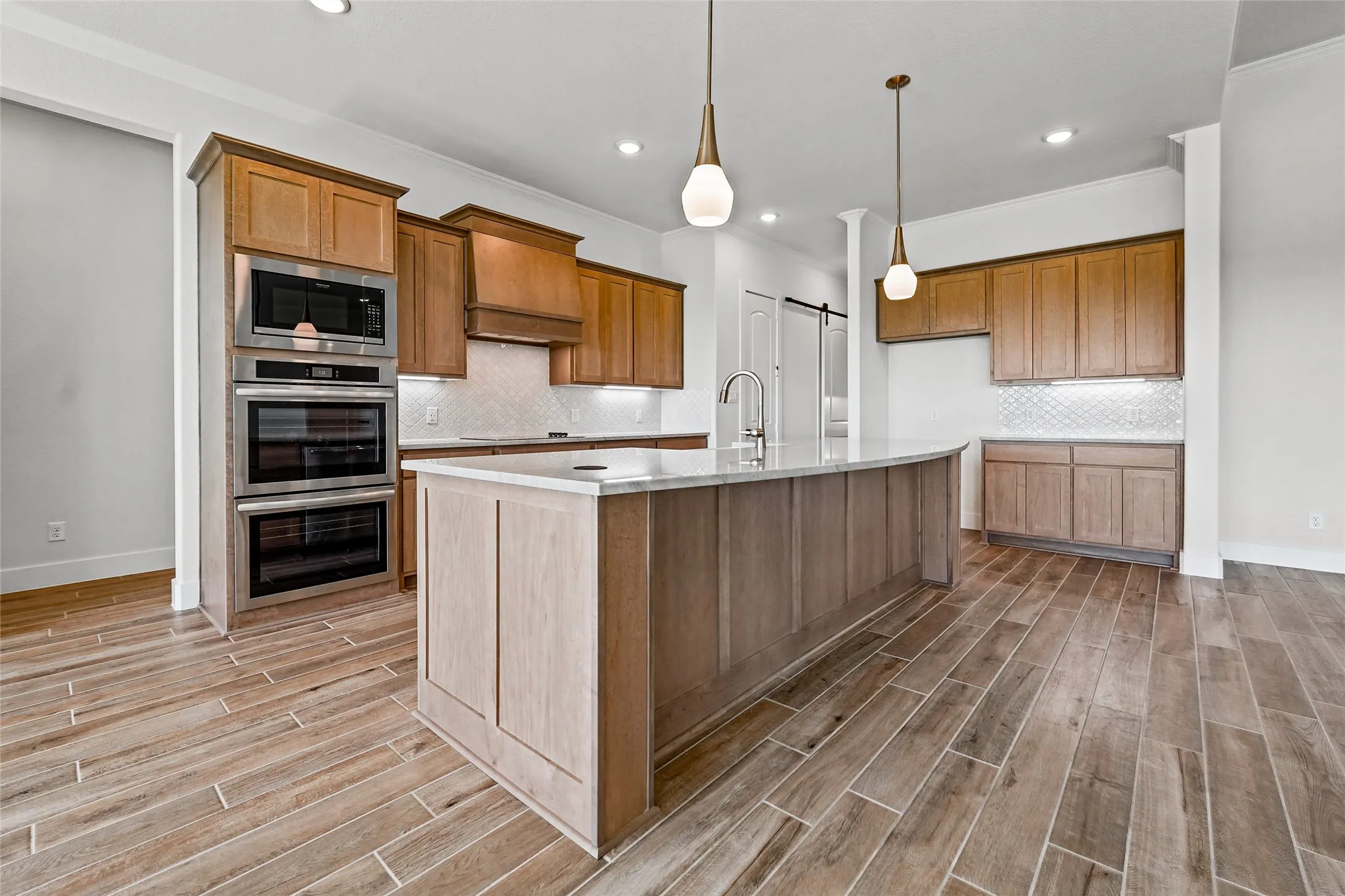 Kitchen featuring wood-finish flooring, custom cabinetry, built-in stainless steel appliances, a large center island with a sink, and pendant lighting