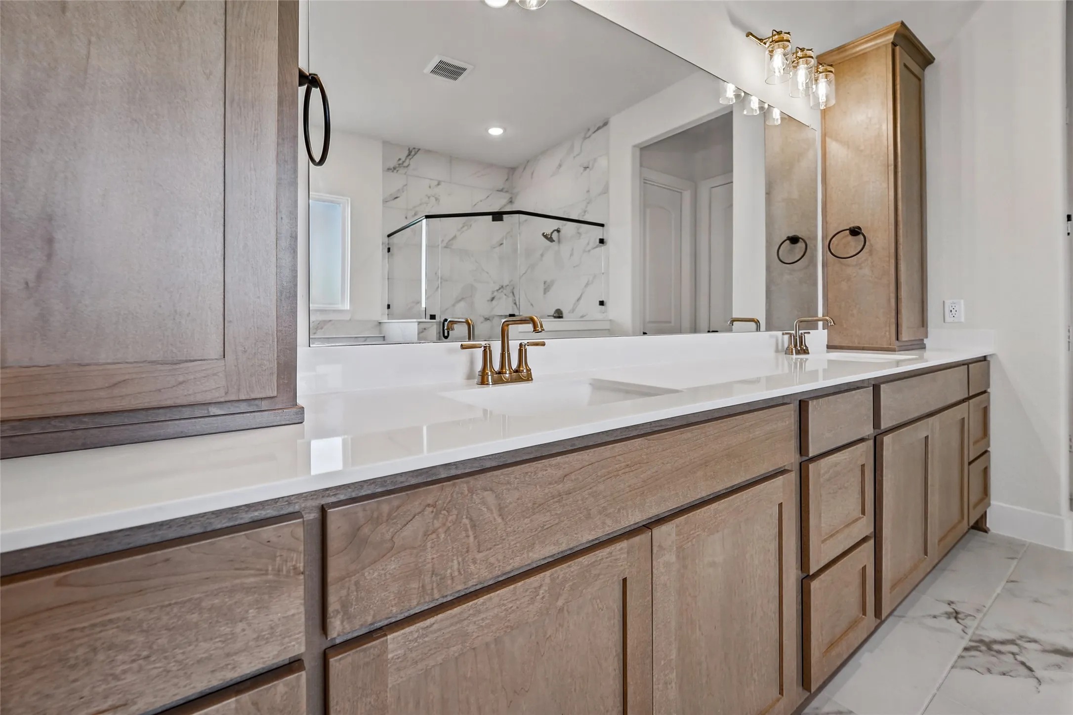 Dual integrated sinks with brass-finish faucets, expansive vanity with wood-finish cabinetry, built-in storage tower, large mirror, and tiled flooring