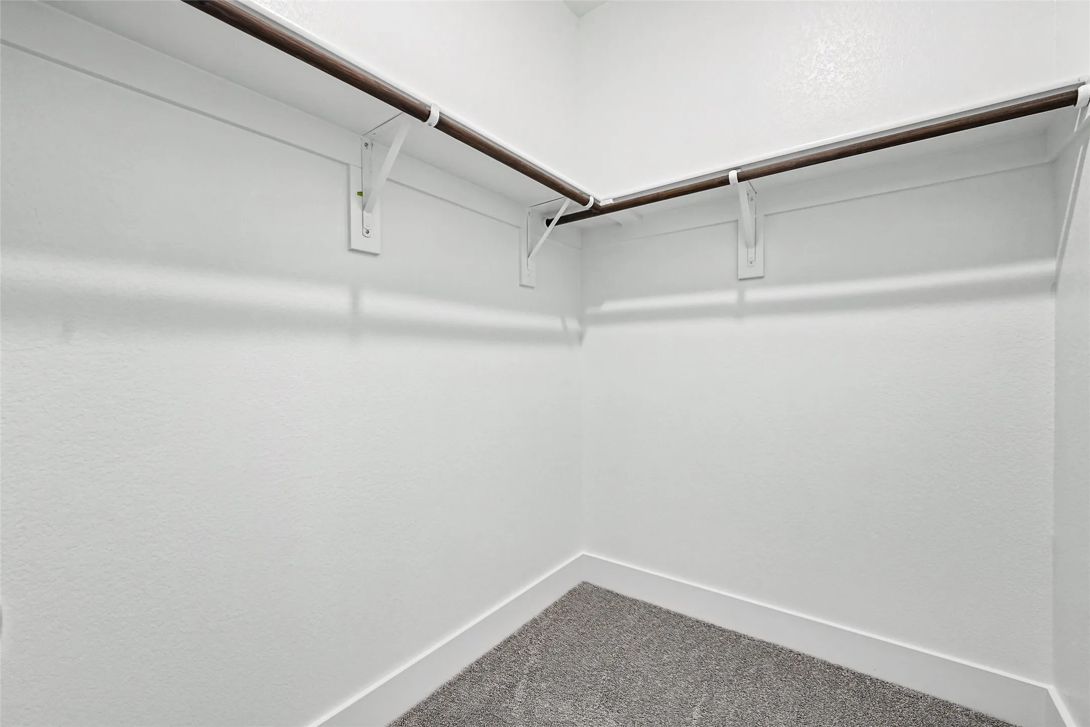 White painted interior with gray carpeted flooring, featuring a built-in hanging rod and shelving