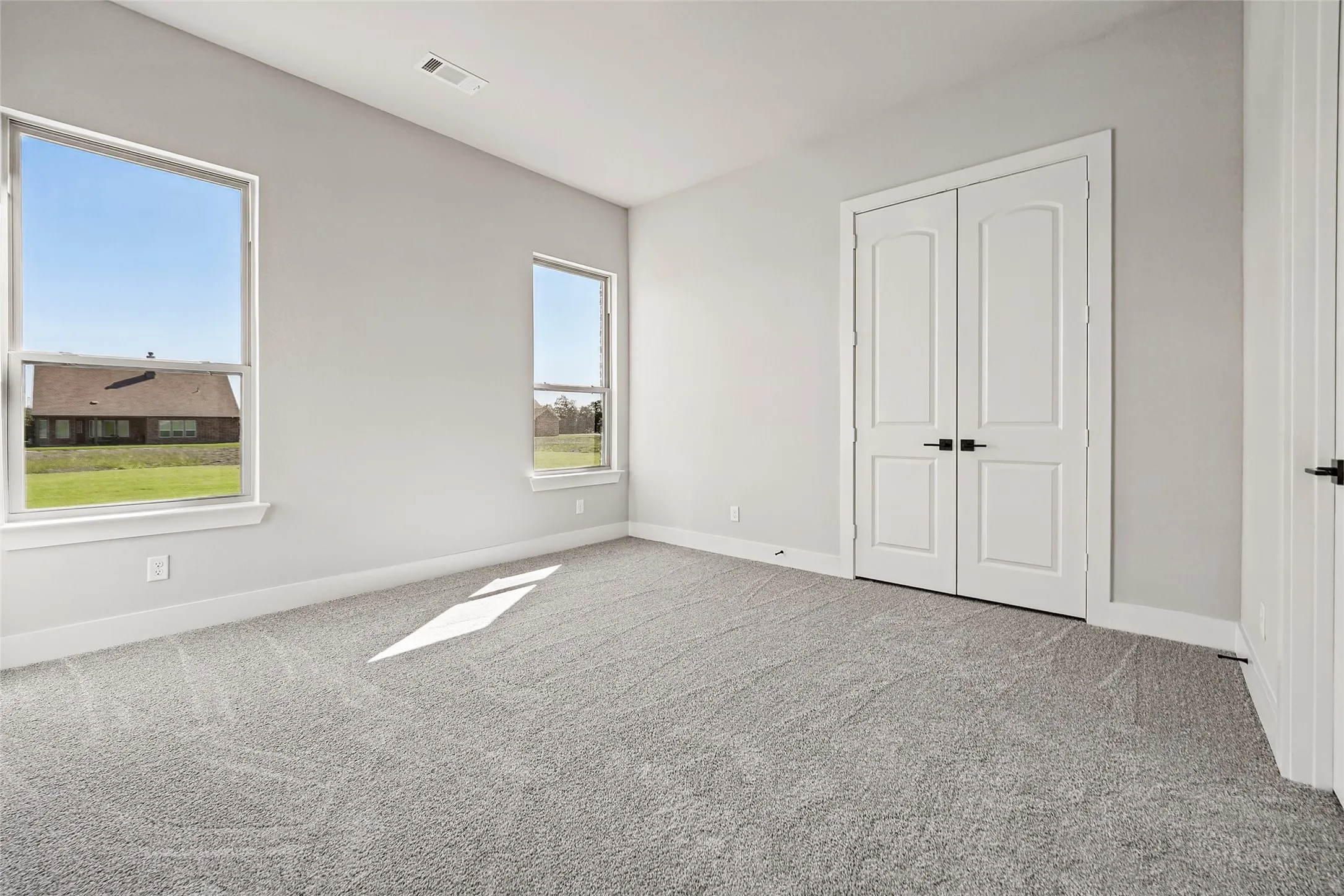 Plush gray carpeting, bright white walls, and a pair of double panel doors with matte black hardware
