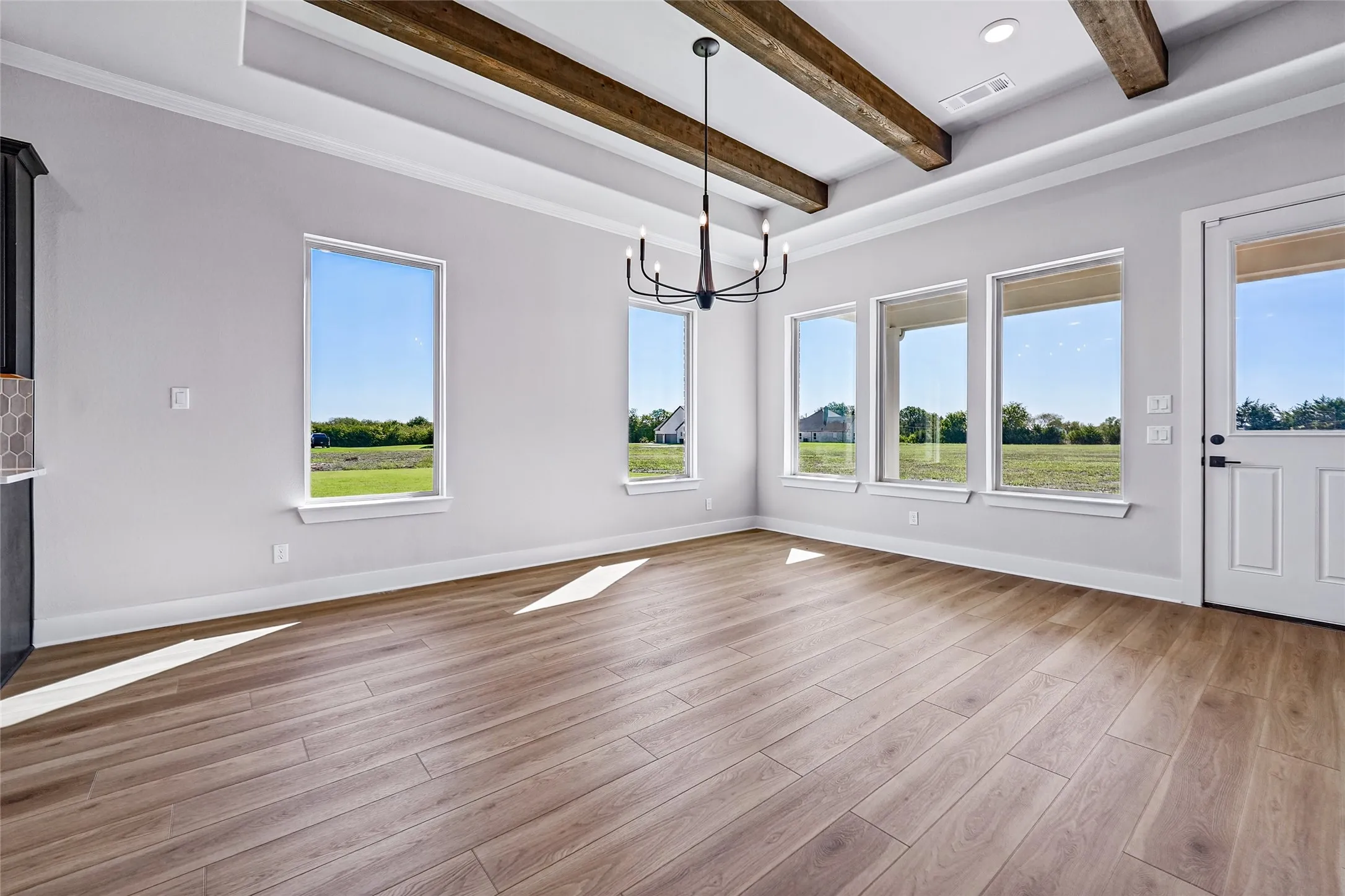 Wood-finish flooring, exposed ceiling beams, recessed lighting, and a modern chandelier