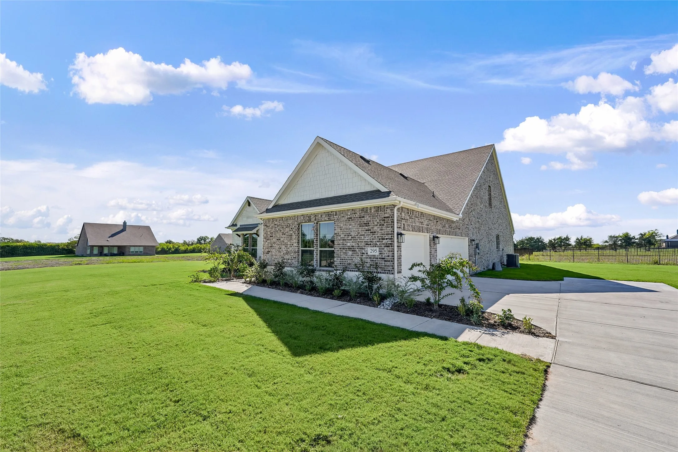 Brick exterior with gabled roofline, concrete driveway, landscaped planting beds, and expansive lawn