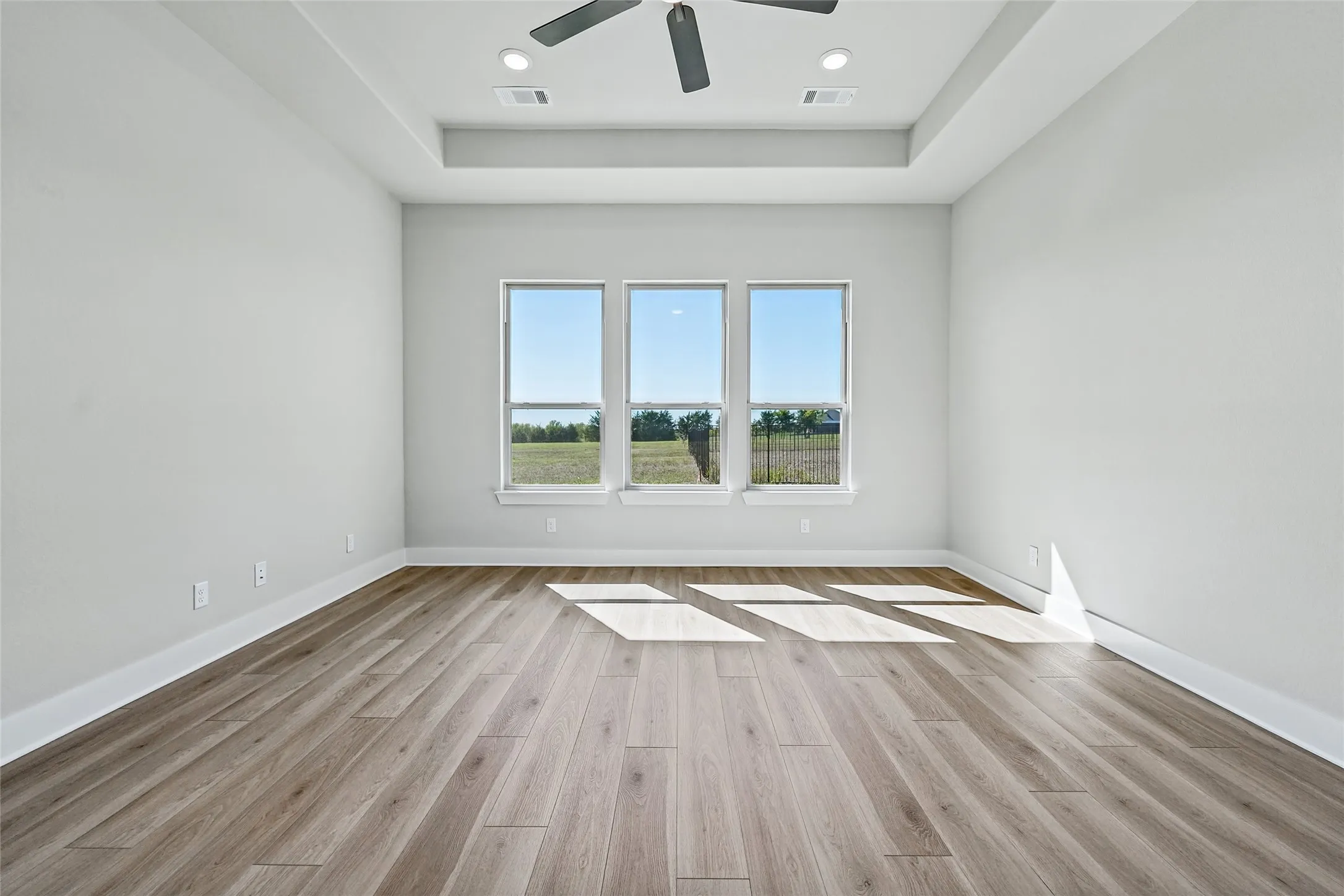 Wood-finish flooring with white baseboards, a tray ceiling, recessed lighting, and a ceiling fan