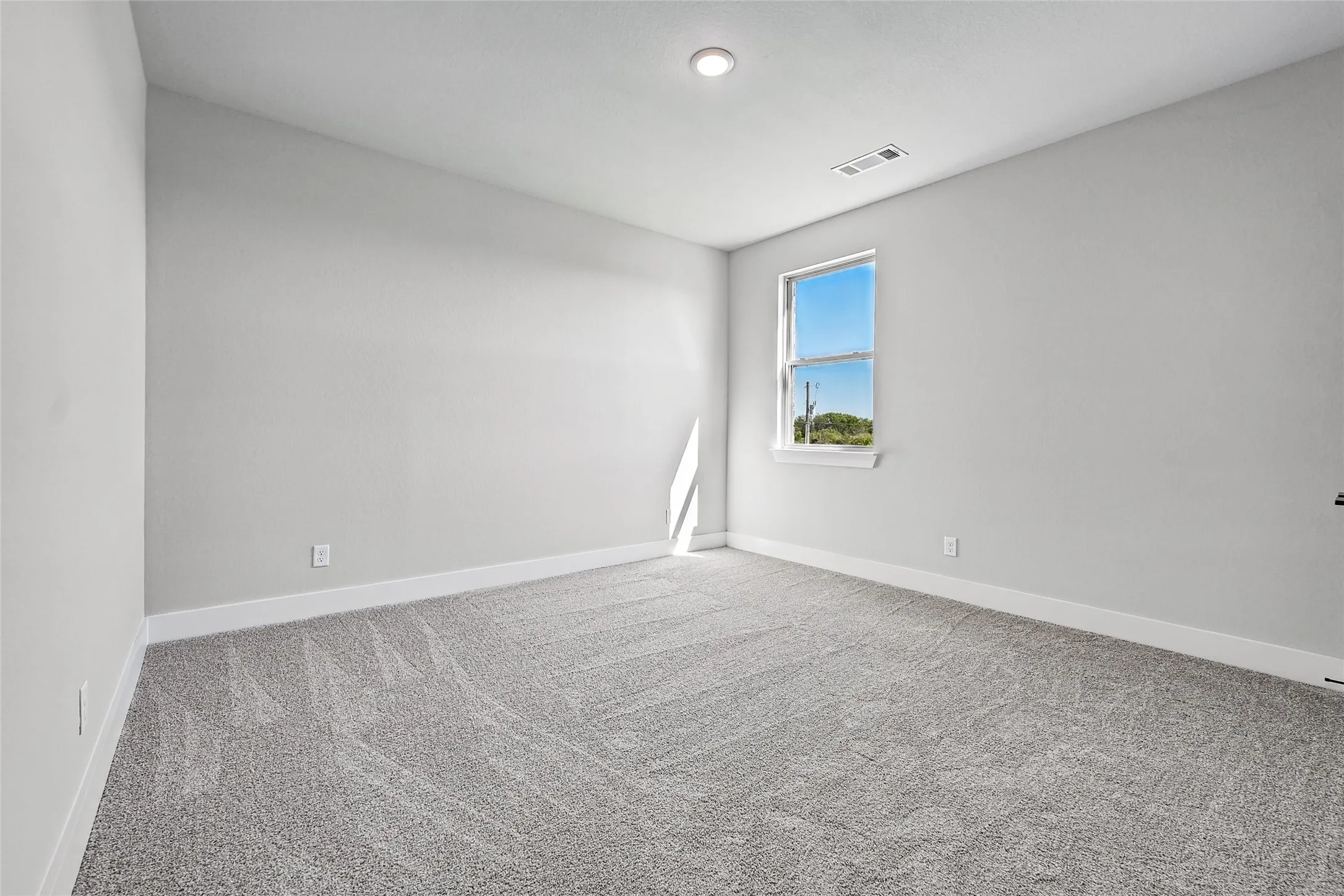 Recessed lighting, light gray wall paint, white trim, gray patterned carpet, and a double-hung window