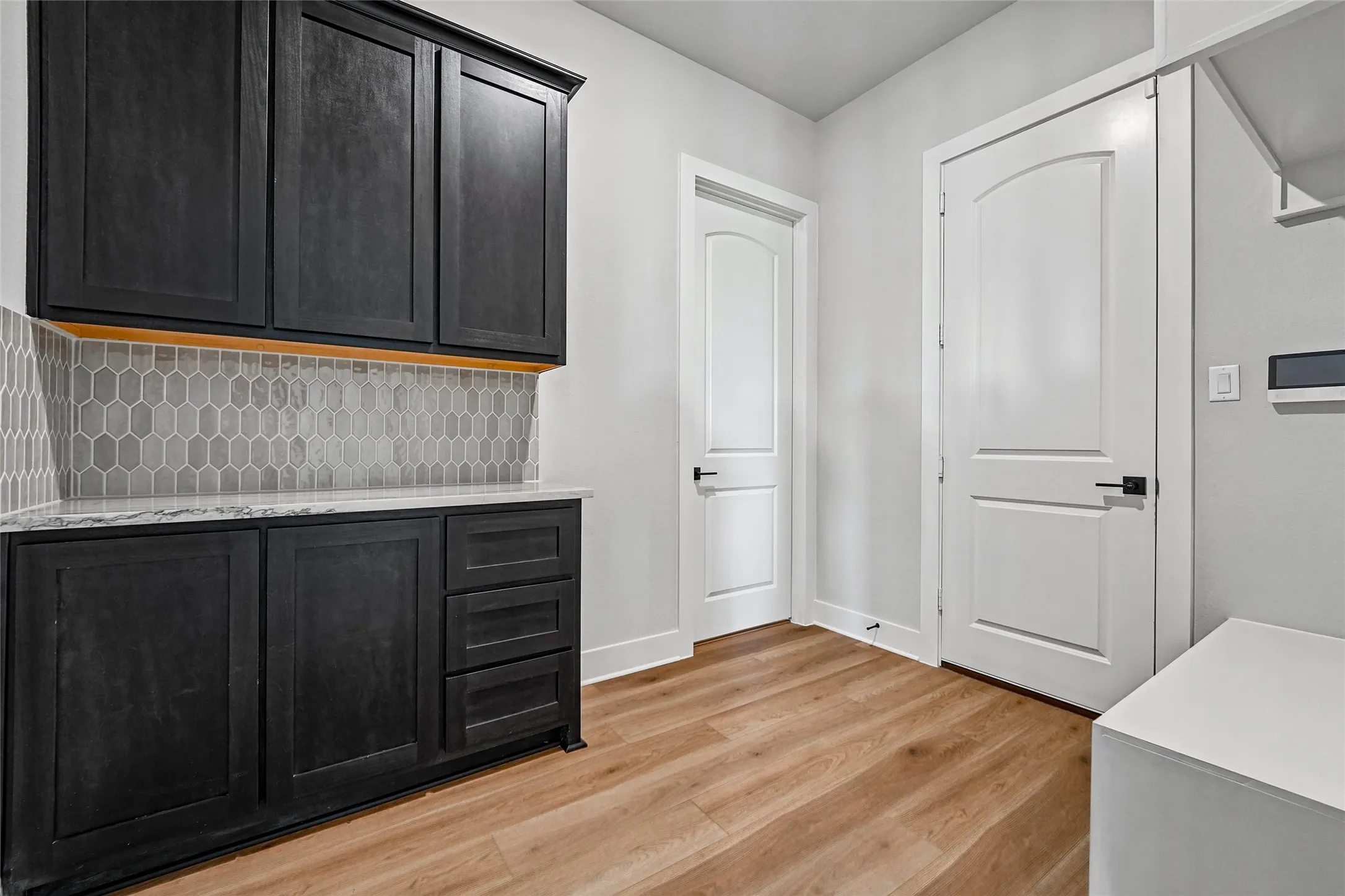 Built-in cabinetry with a stone countertop, hexagonal tile backsplash, and light wood-finish flooring