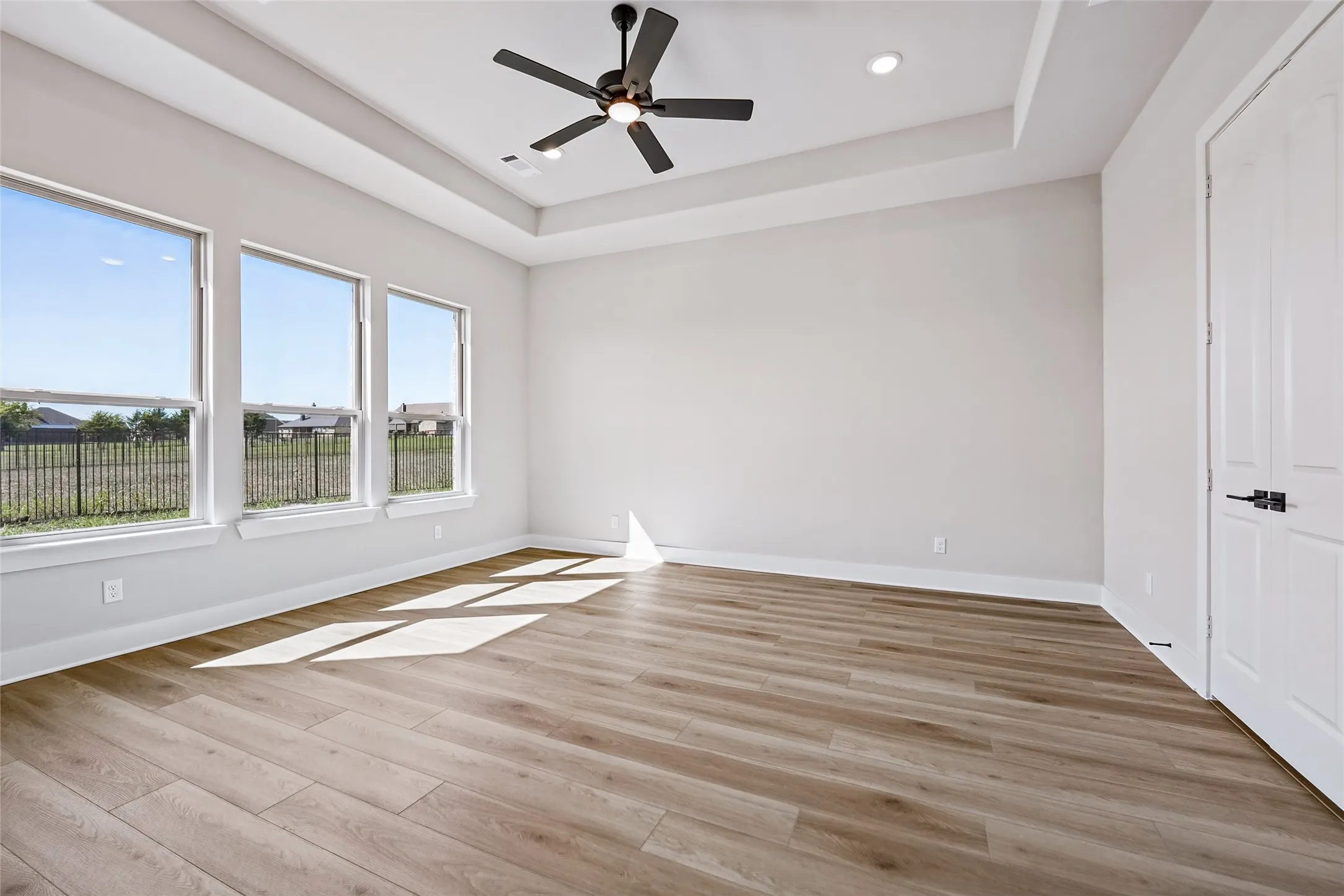 Tray ceiling with recessed lighting and a ceiling fan, wood-finish flooring, and multiple windows