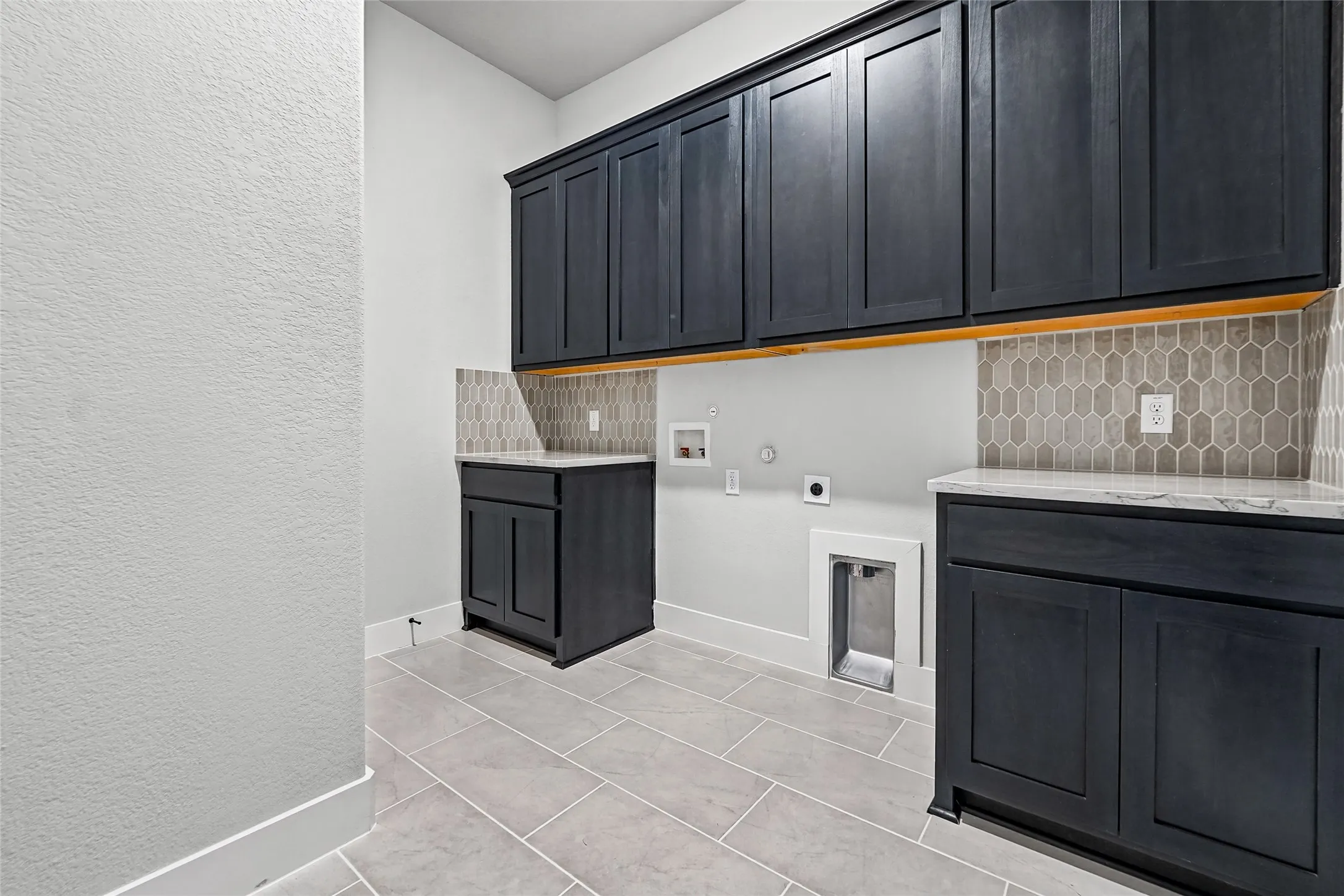Laundry area featuring gray shaker cabinetry, light-toned countertops, and a gray geometric tile backsplash