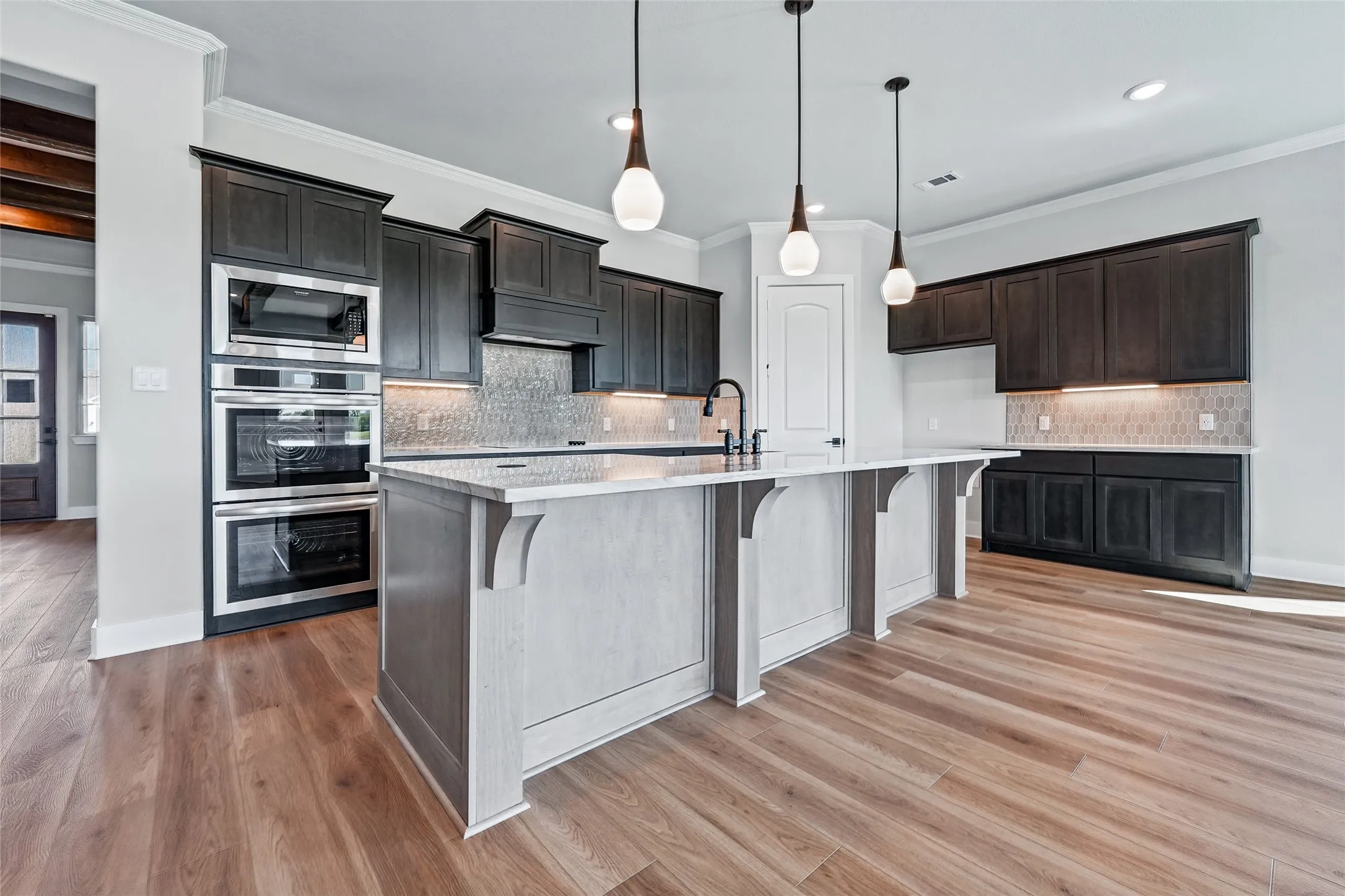 Spacious kitchen featuring wood-finish flooring, dark wood cabinetry, a large kitchen island with a light countertop, and integrated stainless steel double ovens