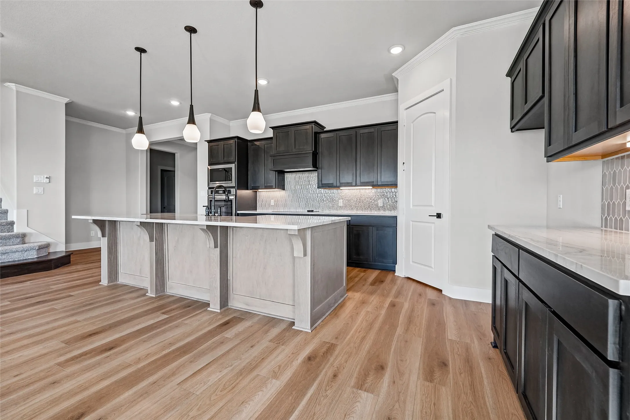 Spacious kitchen featuring a large island, wood-finish flooring, dark cabinetry, light countertops, and a mosaic tile backsplash