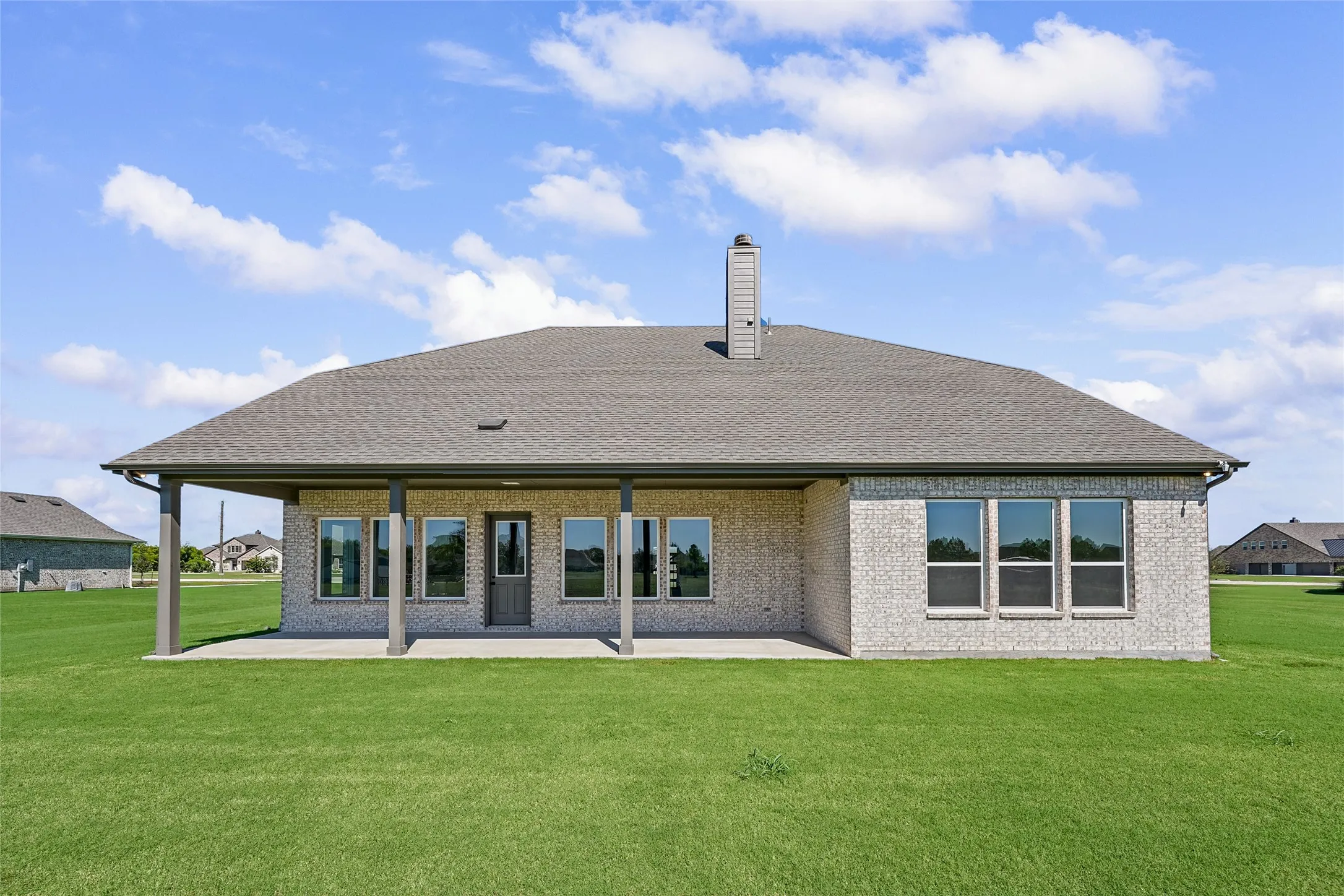 Expansive green lawn, covered patio, brick exterior, multiple windows, and a shingled roof
