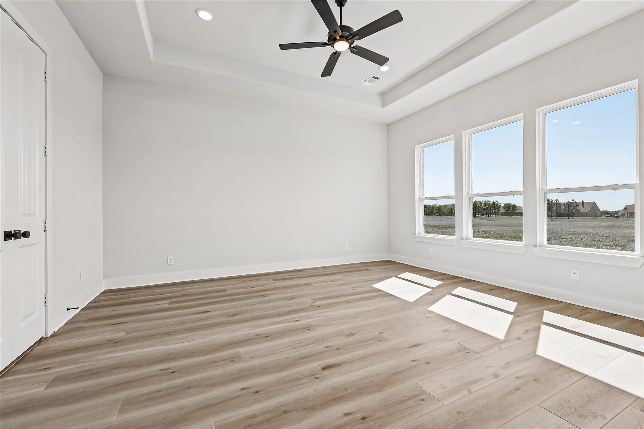 Tray ceiling with recessed lighting, ceiling fan, wood-finish flooring, and multiple windows
