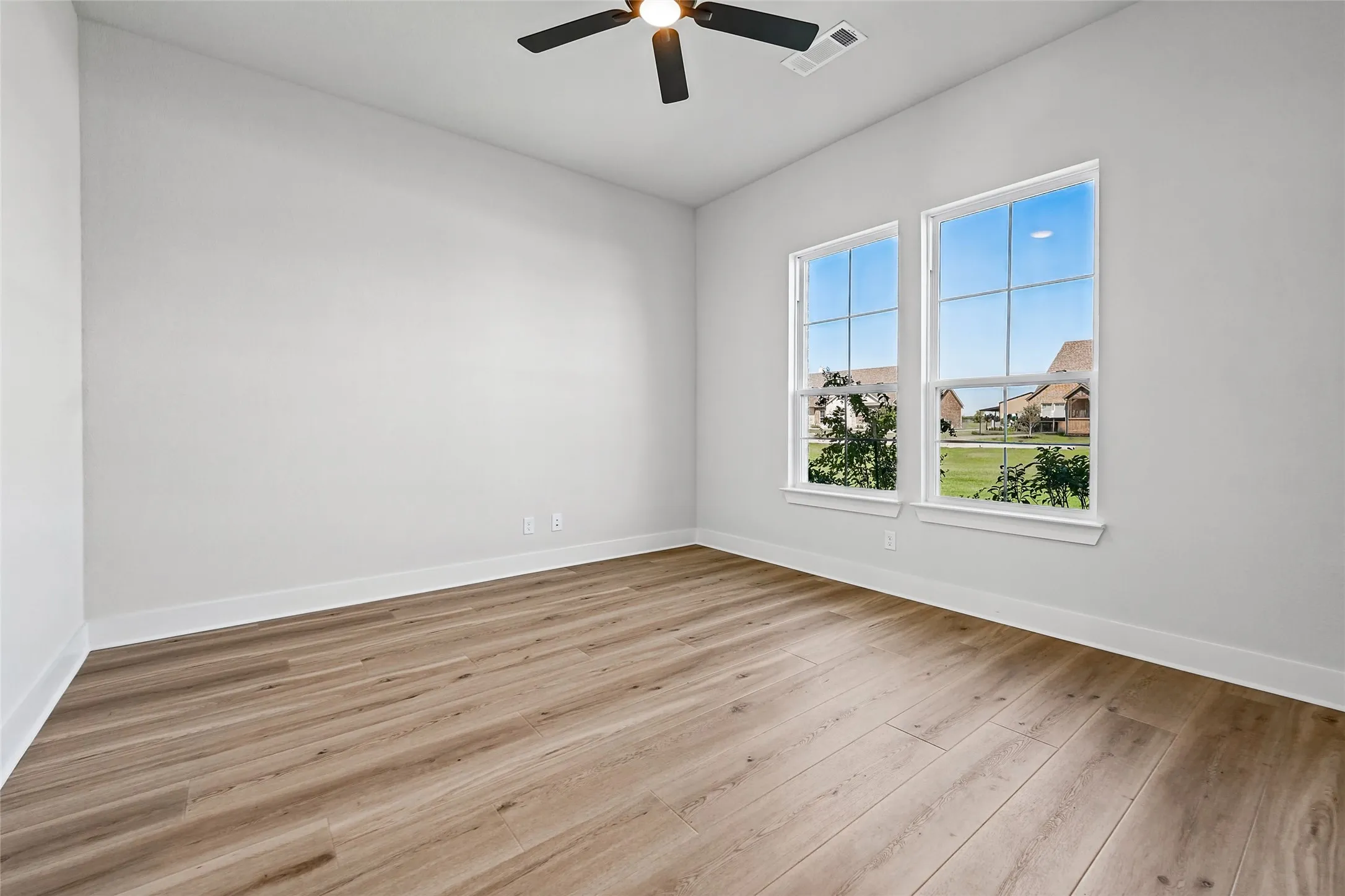 Light-filled room featuring two multi-pane windows, wood-finish flooring, a ceiling fan with integrated lighting, and neutral wall tones