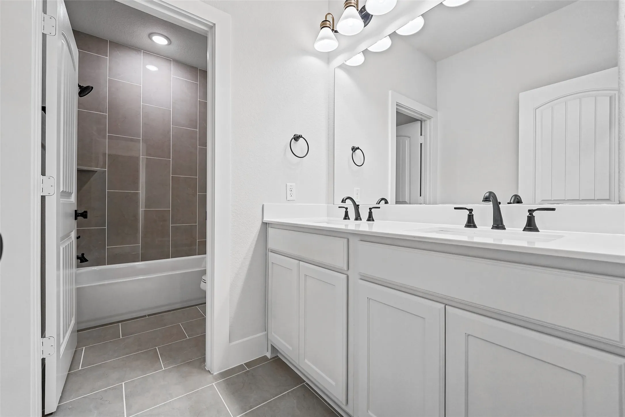 Dual sink vanity with matte black fixtures and white cabinetry, a large mirror, and tile flooring