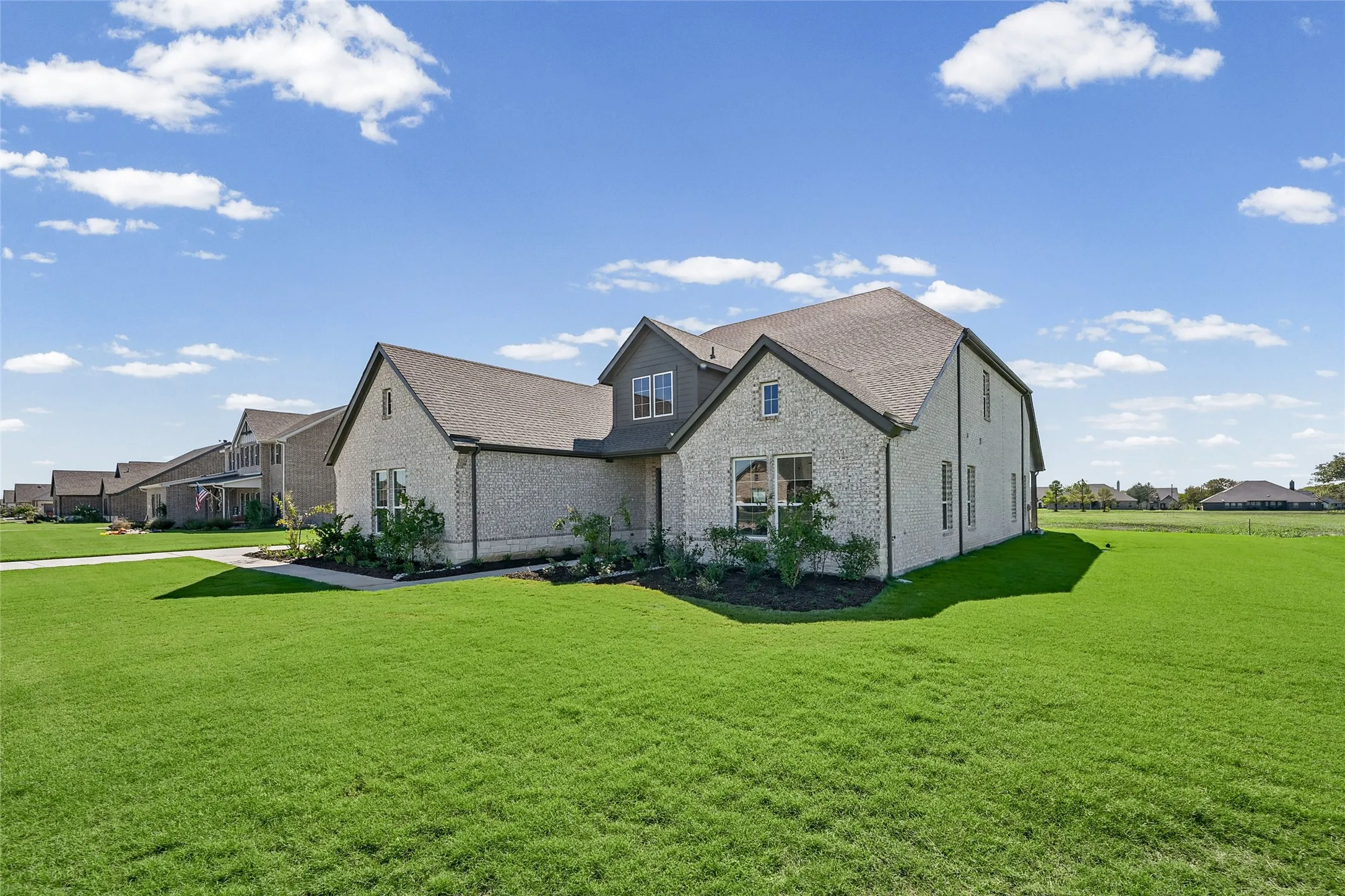 Expansive green lawn surrounding a light brick exterior with dark trim and a dark shingled roof