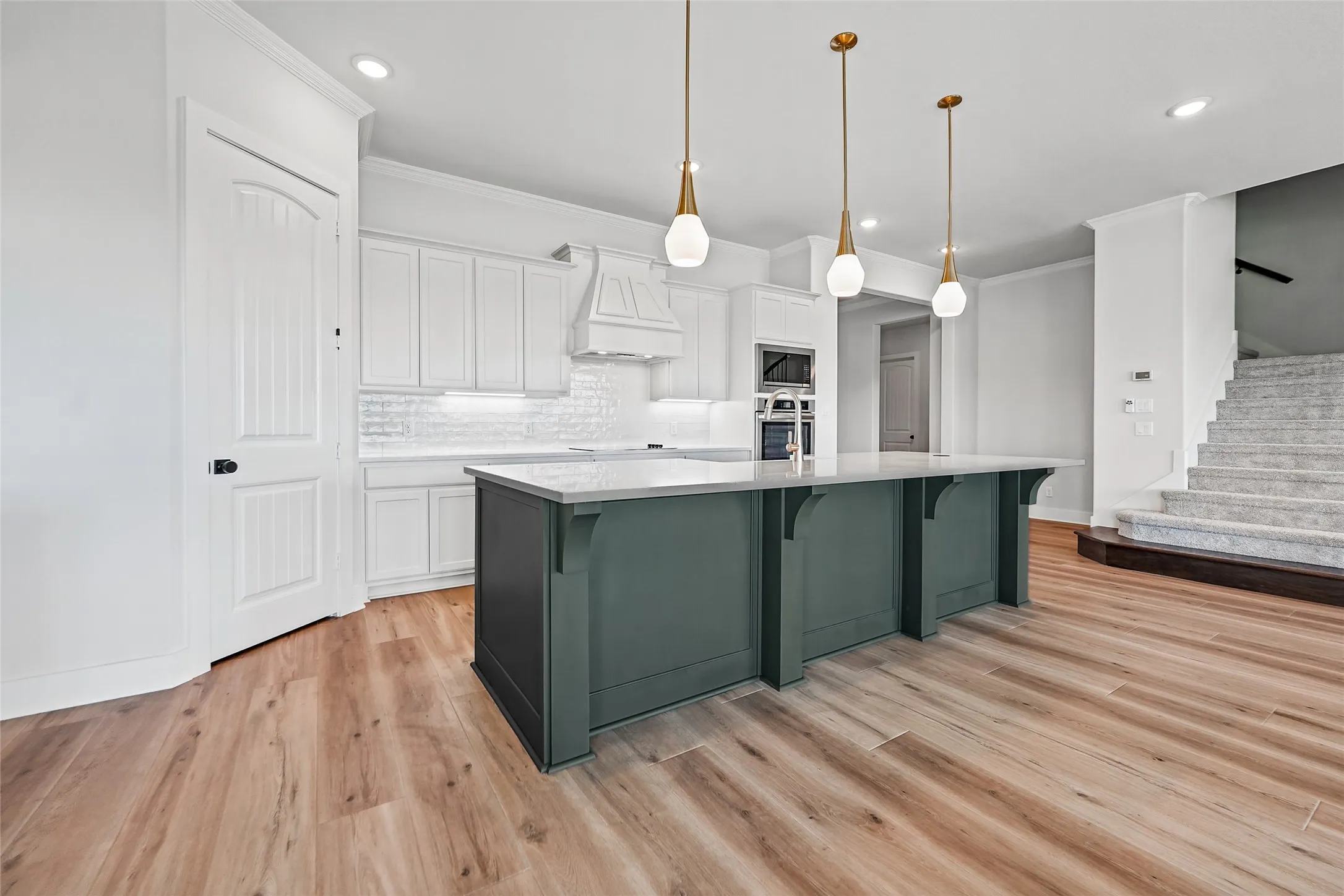 Kitchen featuring a large island with accent cabinetry, integrated stainless steel appliances, light wood-finish flooring, and pendant lighting